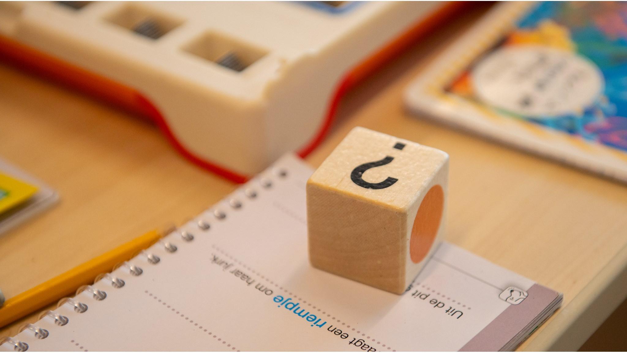 Basisschool De Poort - school met de Bijbel in Ten Boer toont een houten dobbelsteen met een vraagteken op een notitieblok. Basisschool De Poort - school met de Bijbel in Ten Boer toont een houten dobbelsteen met een vraagteken op een notitieblok.