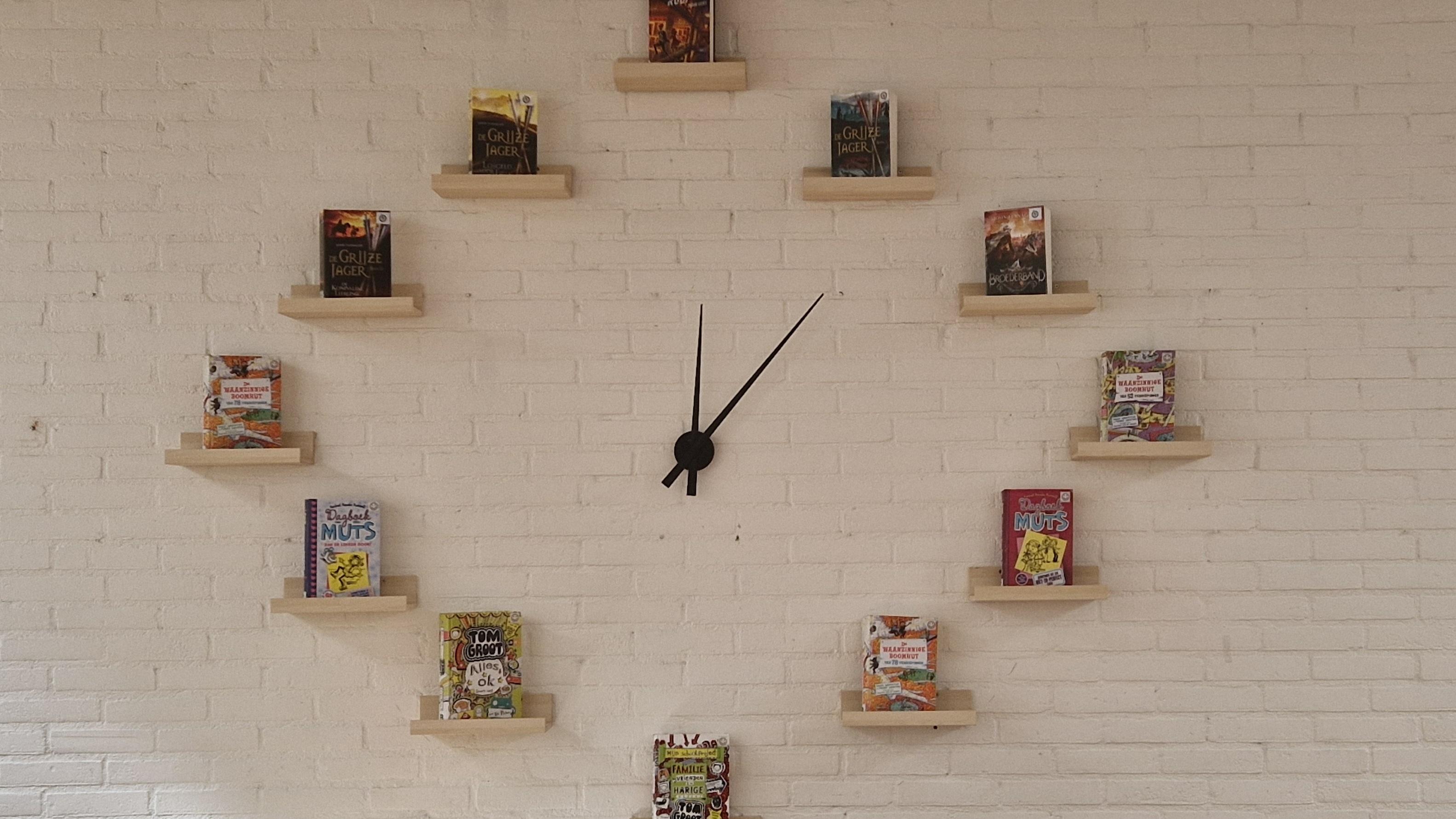 Boekenplank in de klas van KC De Elzenhof in Hardenberg, waarin boeken in de vorm van een klok zijn geplaatst. Boekenplank in de klas van KC De Elzenhof in Hardenberg, waarin boeken in de vorm van een klok zijn geplaatst.