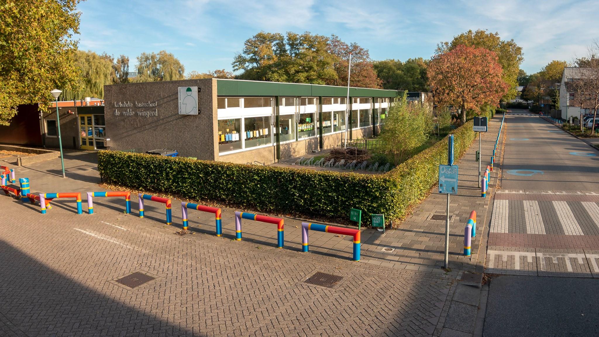 De afbeelding toont de basisschool de Wilde Wingerd in Maarssen met kleurrijke verkeerspaaltjes en een uitnodigende omgeving. De afbeelding toont de basisschool de Wilde Wingerd in Maarssen met kleurrijke verkeerspaaltjes en een uitnodigende omgeving.
