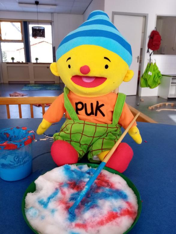 De afbeelding toont een kleurrijke pop genaamd Puk die aan een tafel zit in CKC Rehoboth in Valthermond. De afbeelding toont een kleurrijke pop genaamd Puk die aan een tafel zit in CKC Rehoboth in Valthermond.