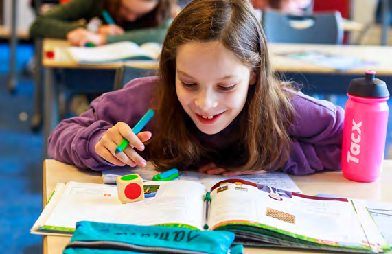 De afbeelding toont een leerling van de Paulus school in Enschede die enthousiast aan het werk is met een boek en schrijfmaterialen. De afbeelding toont een leerling van de Paulus school in Enschede die enthousiast aan het werk is met een boek en schrijfmaterialen.