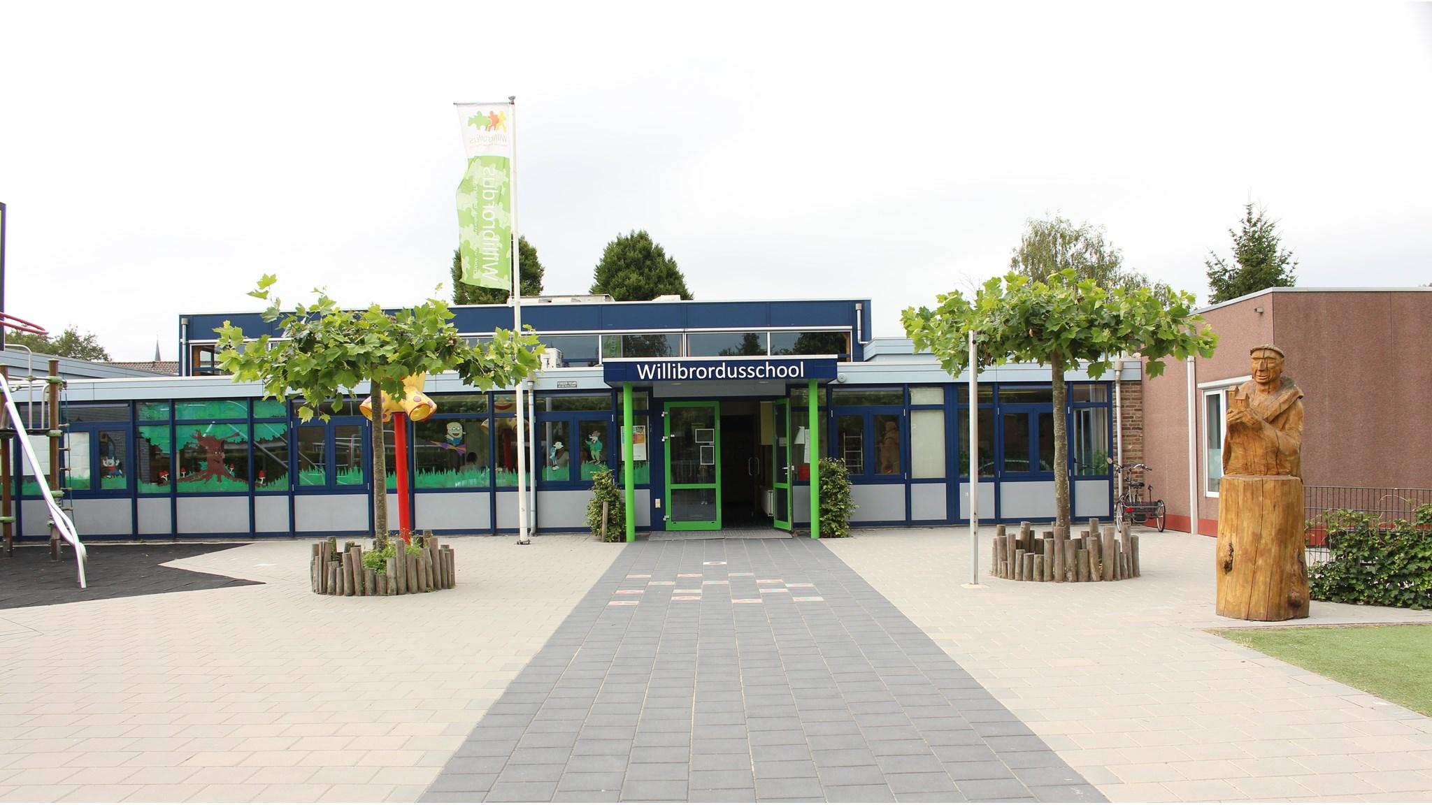 De entree van de Willibrordusschool in Breukelen, met een schoolplein en een houten beeld. De entree van de Willibrordusschool in Breukelen, met een schoolplein en een houten beeld.