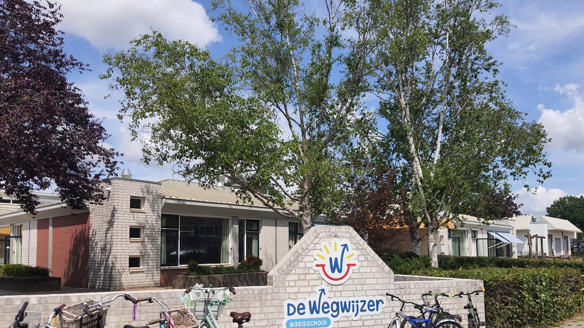 De ingang van Basisschool De Wegwijzer in Sint-Michielsgestel, met fietsen en groene bomen op de achtergrond. De ingang van Basisschool De Wegwijzer in Sint-Michielsgestel, met fietsen en groene bomen op de achtergrond.