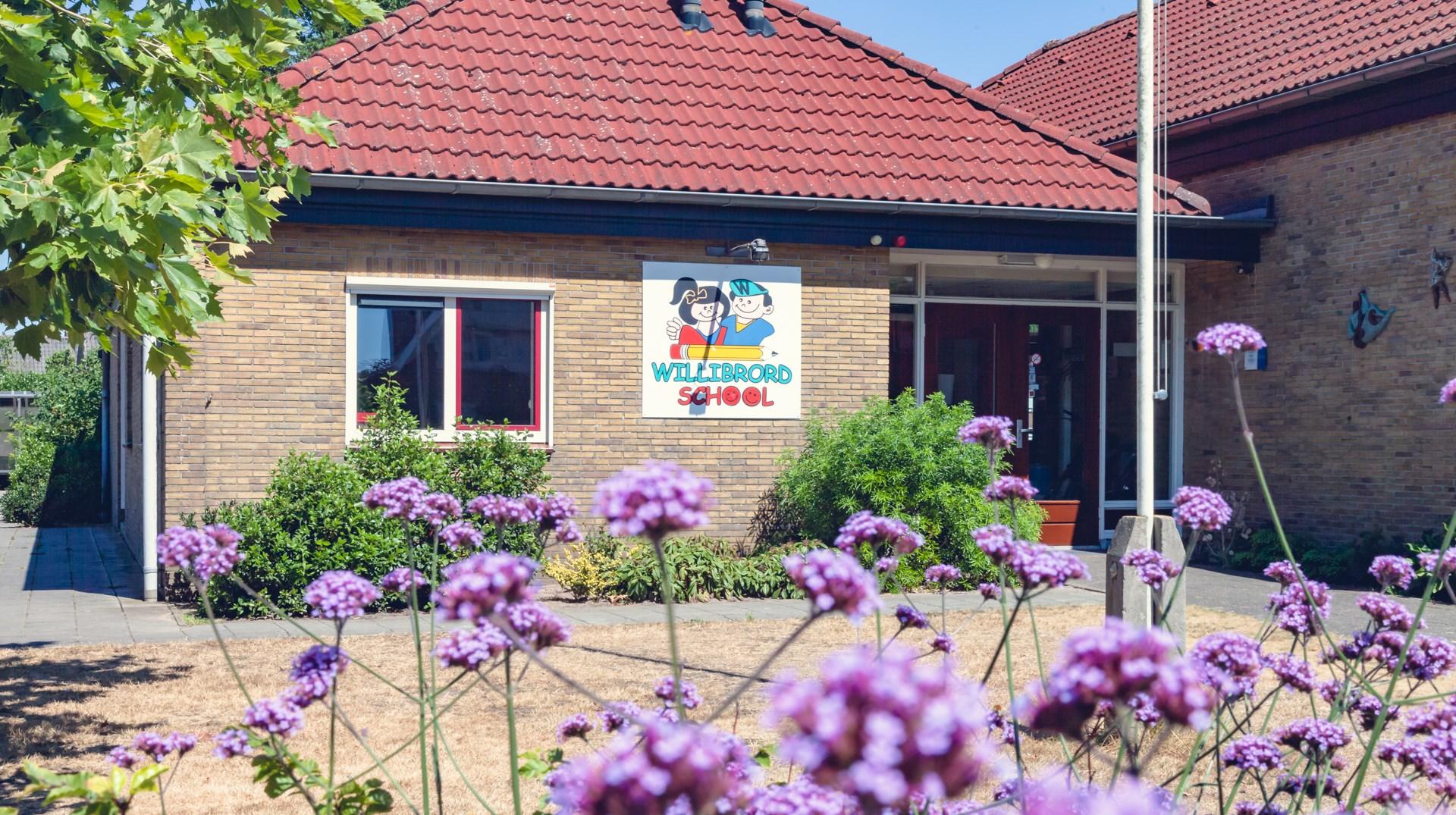 De voorzijde van de Willibrord School in Denekamp met kleurrijke bloemen op de voorgrond. De voorzijde van de Willibrord School in Denekamp met kleurrijke bloemen op de voorgrond.