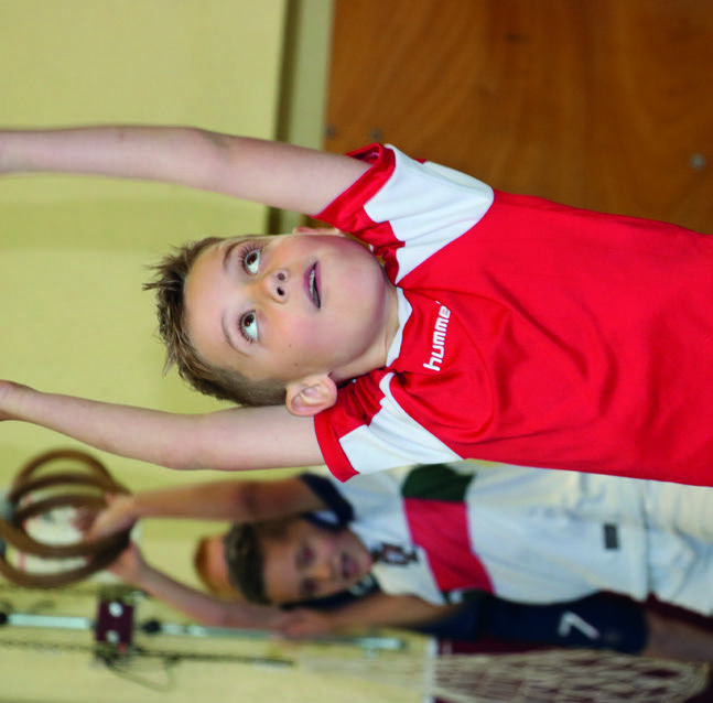 Dit is een afbeelding van een jongen in een rode sportoutfit die blij gymnastiek doet op Christelijke Basisschool De Bron in Wezep.