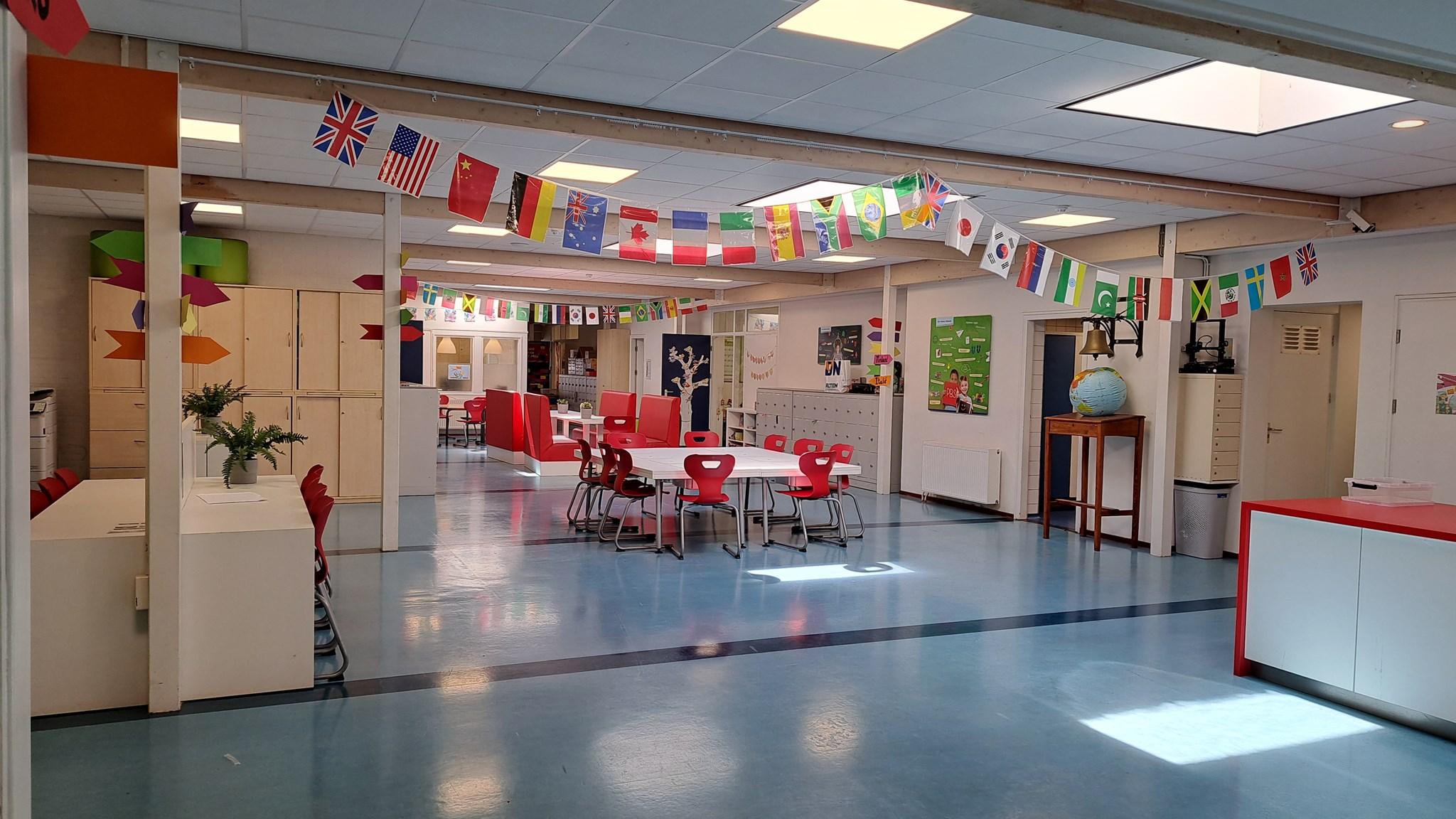 Dit is een kleurrijke ruimte in OBS Willem Wilmink in Enschede, vol met vlaggen en meubels voor samenwerking en leren. Dit is een kleurrijke ruimte in OBS Willem Wilmink in Enschede, vol met vlaggen en meubels voor samenwerking en leren.