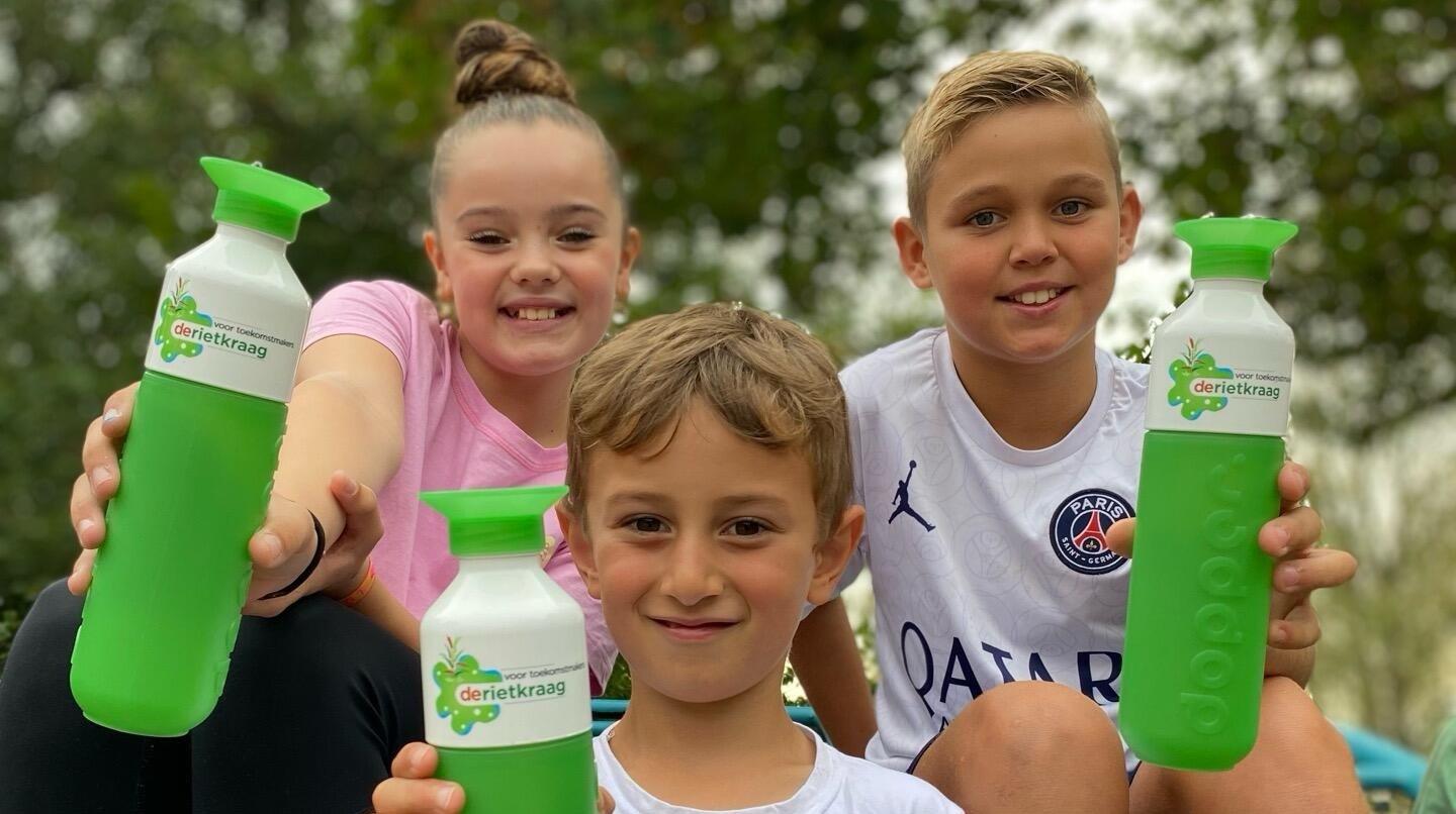 Drie blije kinderen houden Dopper-flessen vast op het schoolplein van Openbare Basisschool De Rietkraag in Oostzaan. Drie blije kinderen houden Dopper-flessen vast op het schoolplein van Openbare Basisschool De Rietkraag in Oostzaan.