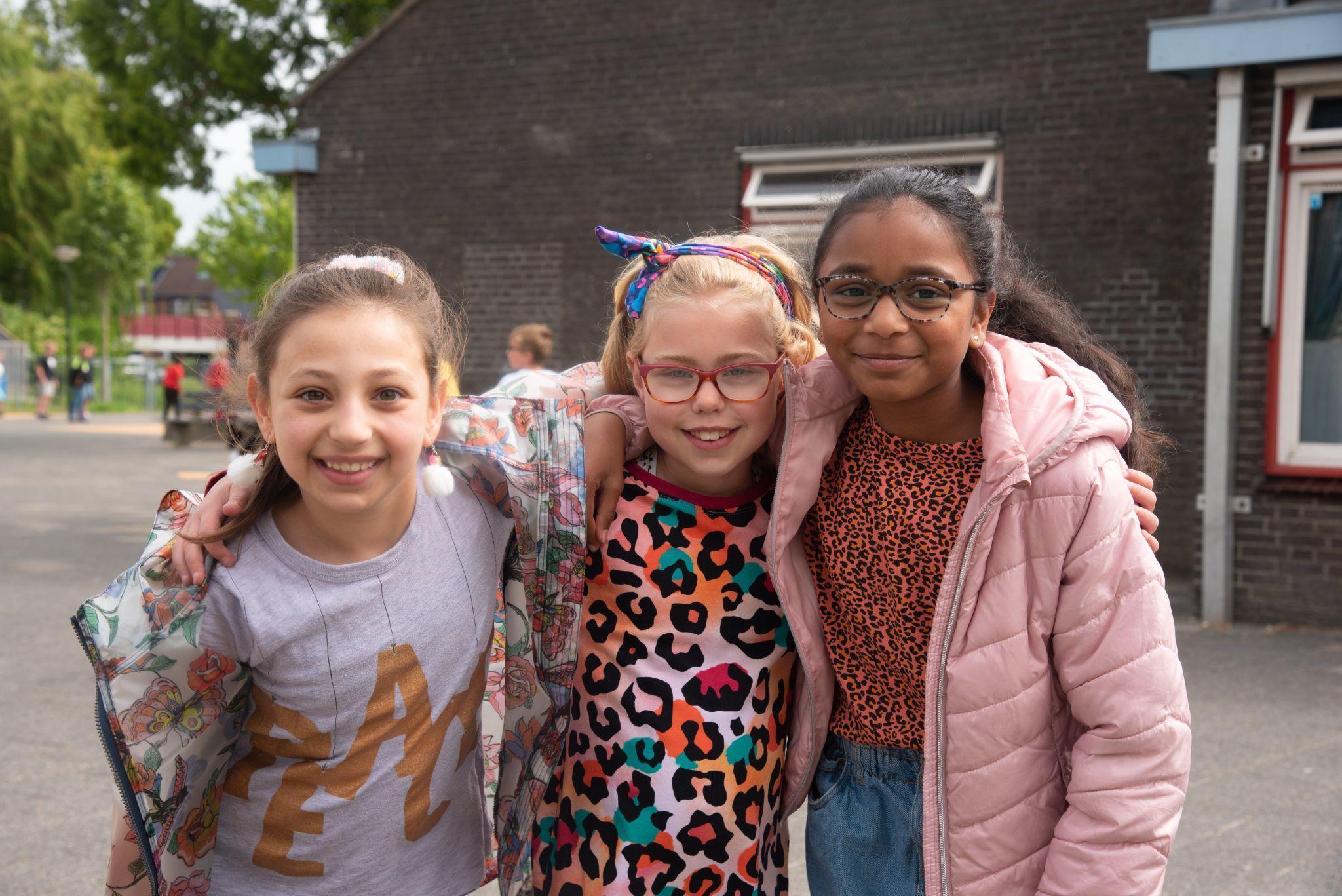Drie blije kinderen poseren samen op het schoolplein van Basisschool Wisperweide in Weesp. Drie blije kinderen poseren samen op het schoolplein van Basisschool Wisperweide in Weesp.