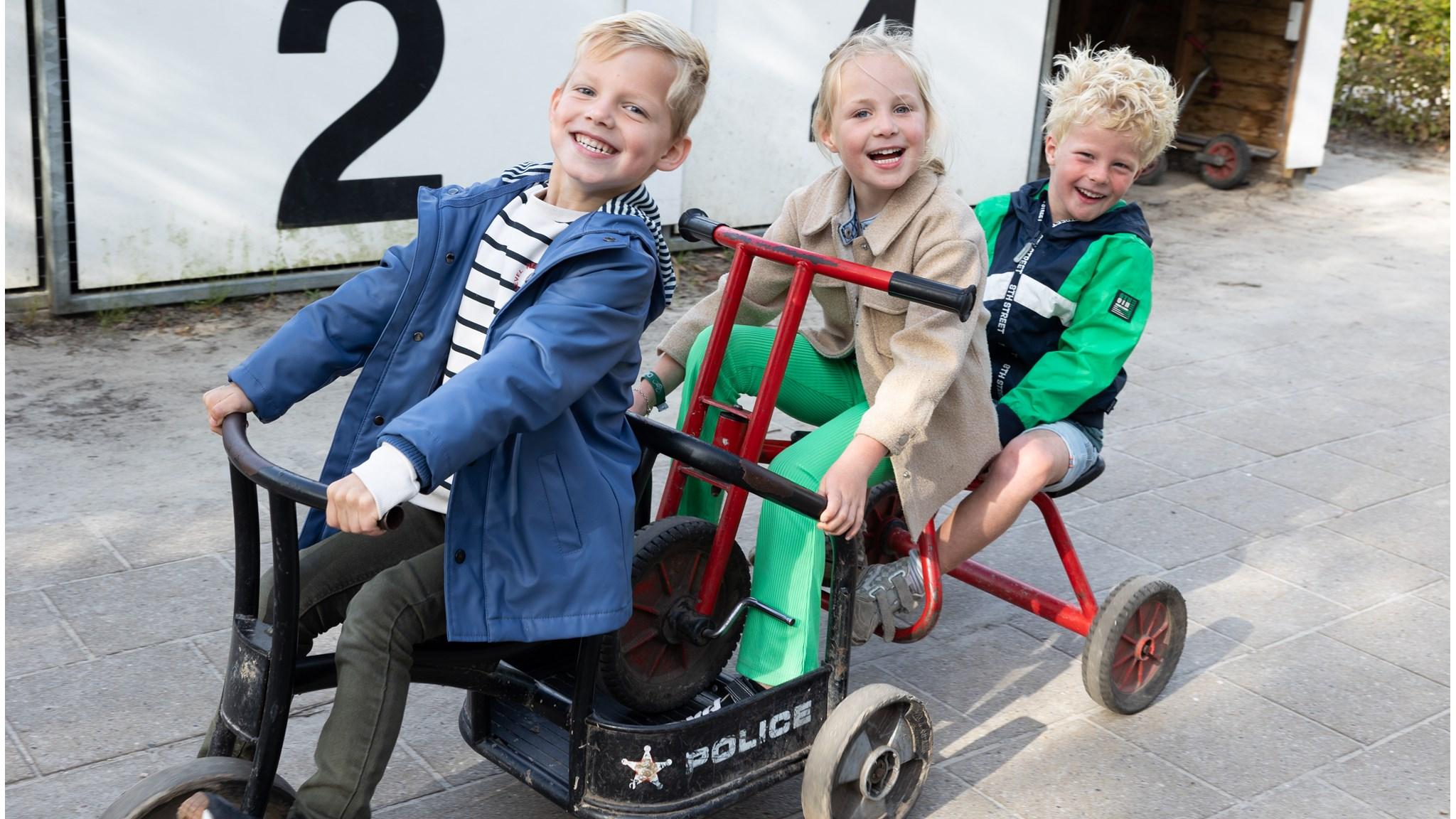 Drie blije kinderen spelen op houten fietsen op het schoolplein van Openbare Basisschool De Twa Fisken in Grou. Drie blije kinderen spelen op houten fietsen op het schoolplein van Openbare Basisschool De Twa Fisken in Grou.