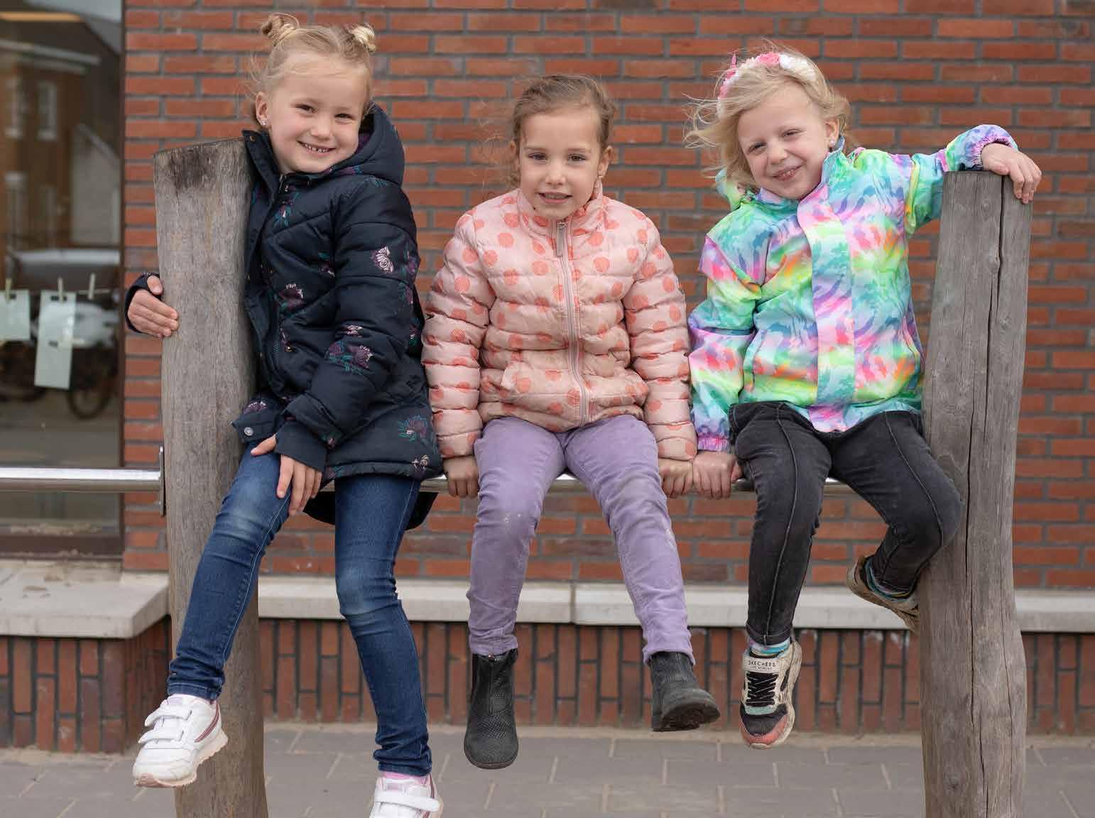 Drie blije kinderen zitten op een speeltoestel op het schoolplein van Het Avontuur in Hoef en Haag.