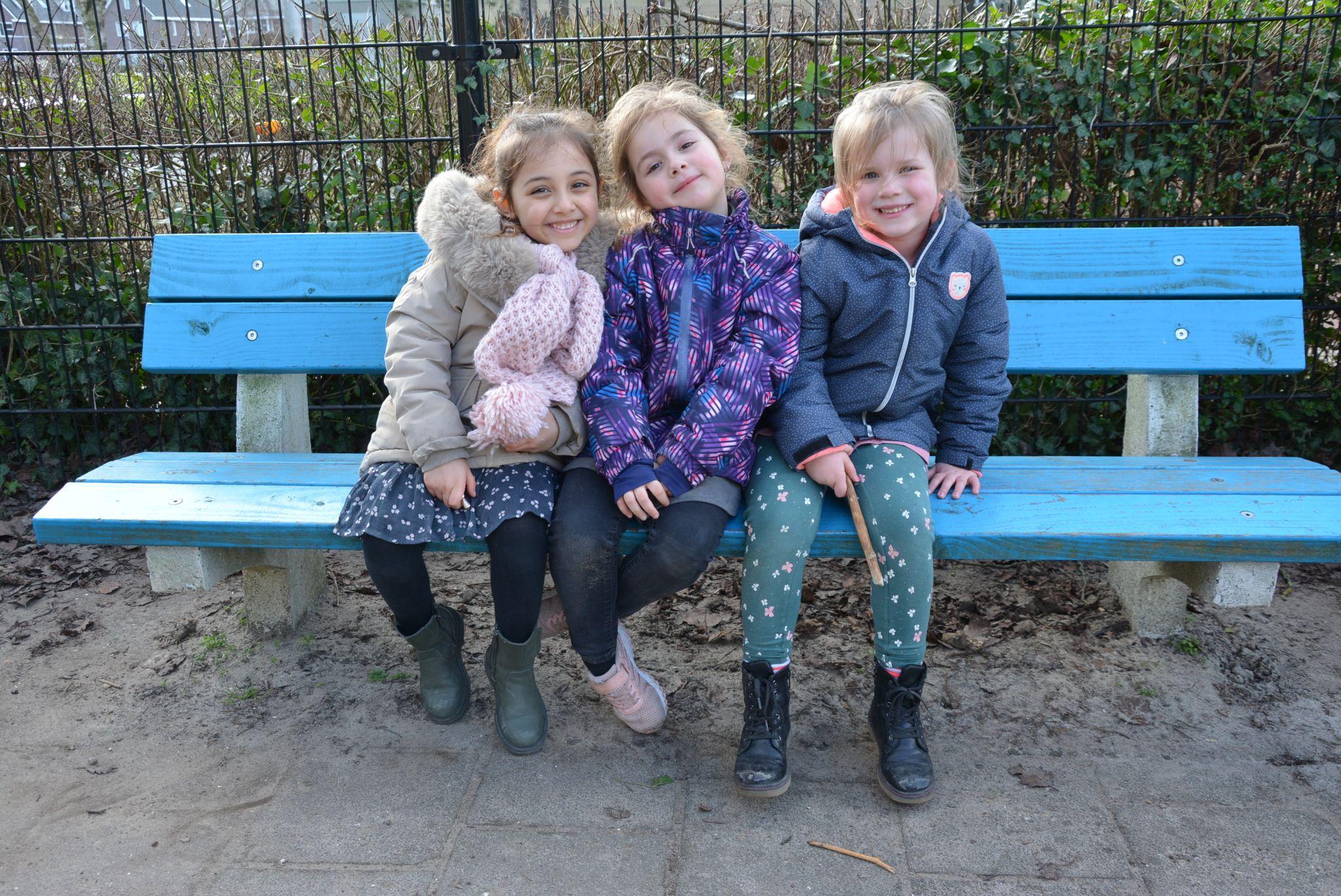 Drie blije kinderen zitten samen op een blauwe bank op het schoolplein van CBS De Klimop in Ridderkerk. Drie blije kinderen zitten samen op een blauwe bank op het schoolplein van CBS De Klimop in Ridderkerk.