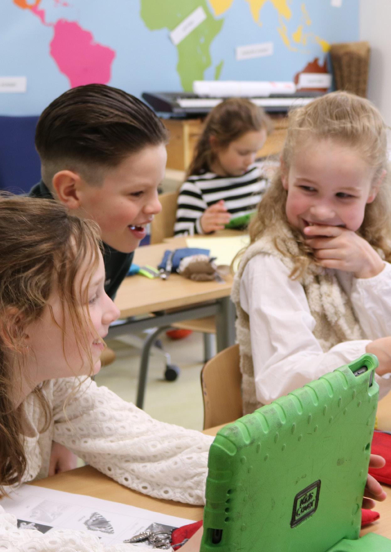 Drie blije leerlingen van Basisschool De Kersentuin in Mierlo werken samen met een tablet in de klas.