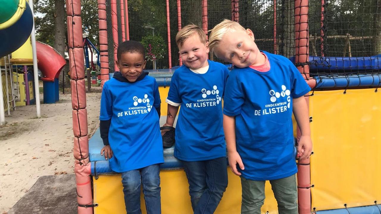 Drie gelukkige kinderen in blauwe T-shirts van Kindcentrum De Klister op het schoolplein in Nieuw-Buinen. Drie gelukkige kinderen in blauwe T-shirts van Kindcentrum De Klister op het schoolplein in Nieuw-Buinen.