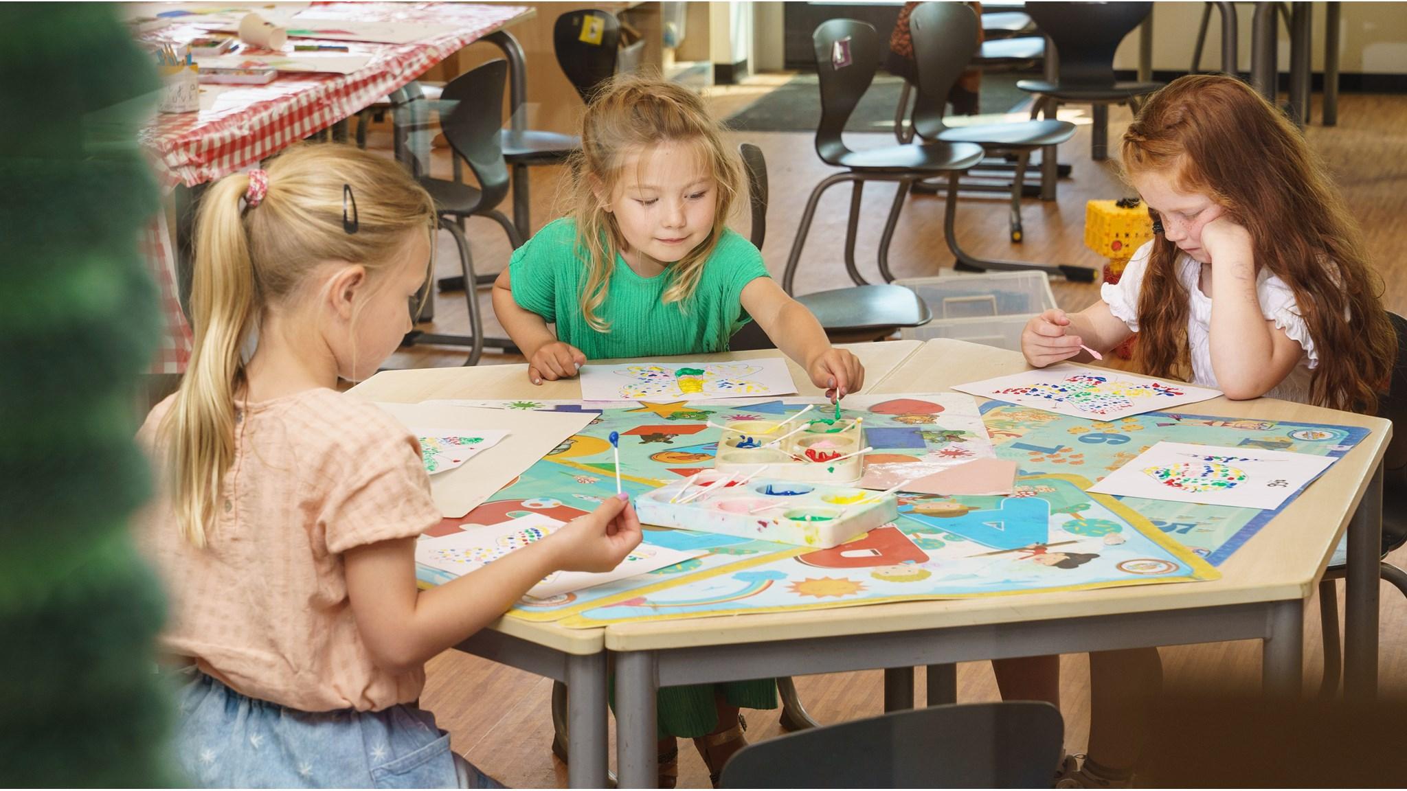 Drie kinderen aan een tafel met kunstprojecten in CKC De Rietzanger in Eelderwolde.