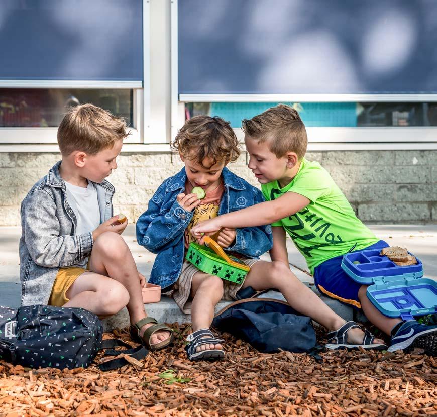 Drie kinderen genieten van hun lunch op het schoolplein van De Parelburcht in Oost-Souburg.