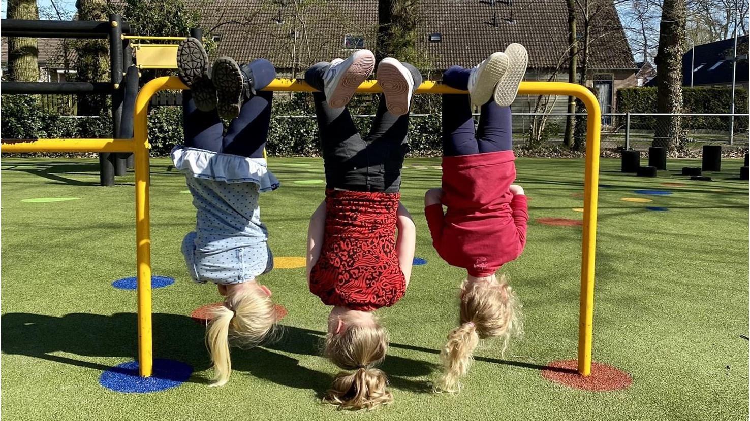 Drie kinderen hangen ondersteboven aan een gele speeltuig in het schoolplein van OBS Gildeschool in Epe. Drie kinderen hangen ondersteboven aan een gele speeltuig in het schoolplein van OBS Gildeschool in Epe.