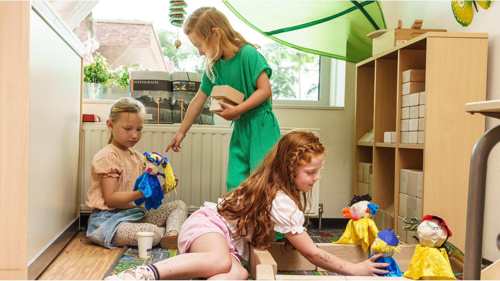 Drie kinderen spelen met zelfgemaakte poppen en blokken in CKC De Rietzanger in Eelderwolde.