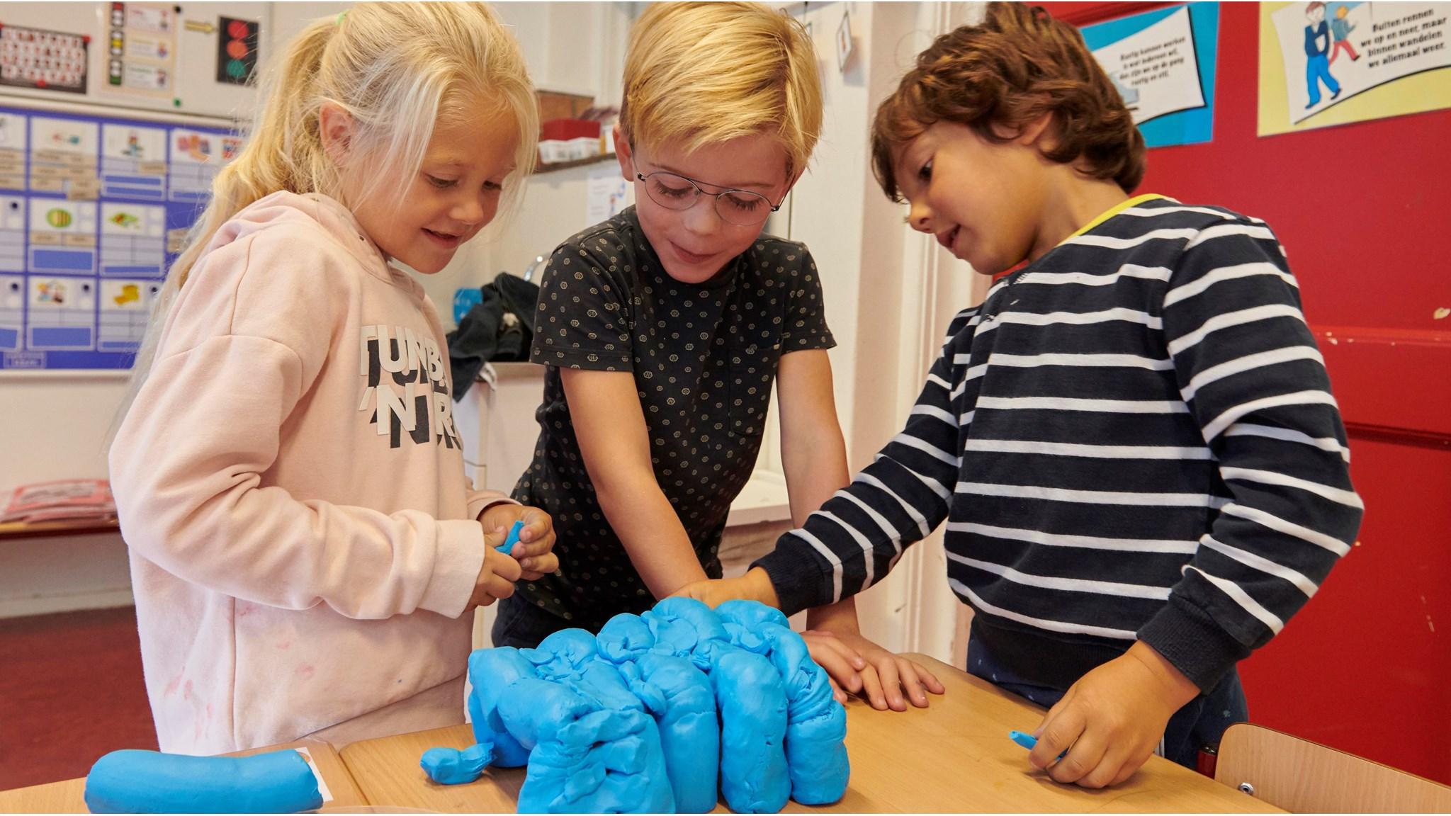 Drie leerlingen van De Beatrixschool in Haarlem spelen samen met blauwe klei in de klas. Drie leerlingen van De Beatrixschool in Haarlem spelen samen met blauwe klei in de klas.