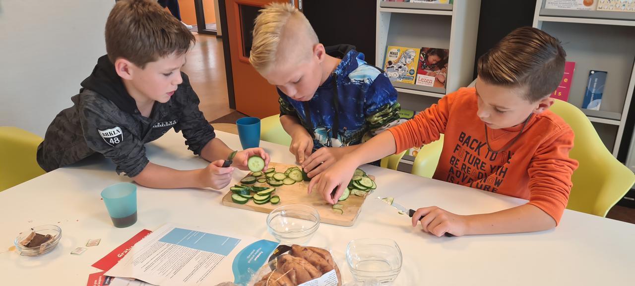 Drie leerlingen van de Rooms Katholieke Basisschool Sint Martinus in Voorst zijn bezig met het snijden van komkommer. Drie leerlingen van de Rooms Katholieke Basisschool Sint Martinus in Voorst zijn bezig met het snijden van komkommer.
