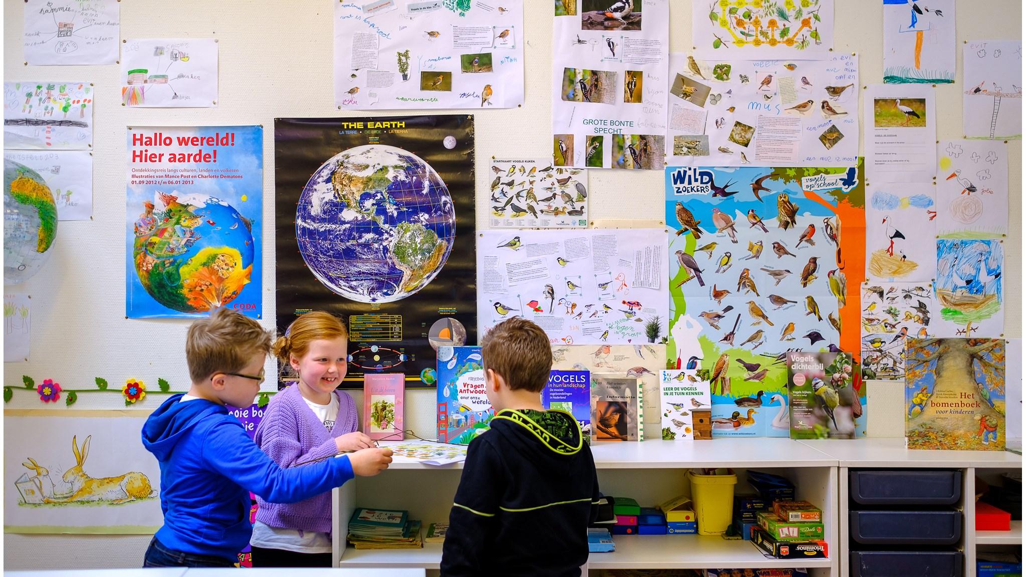 Drie leerlingen van PCBO De Ploeg in Apeldoorn bekijken educatieve materialen en kunstwerken in een klaslokaal. Drie leerlingen van PCBO De Ploeg in Apeldoorn bekijken educatieve materialen en kunstwerken in een klaslokaal.