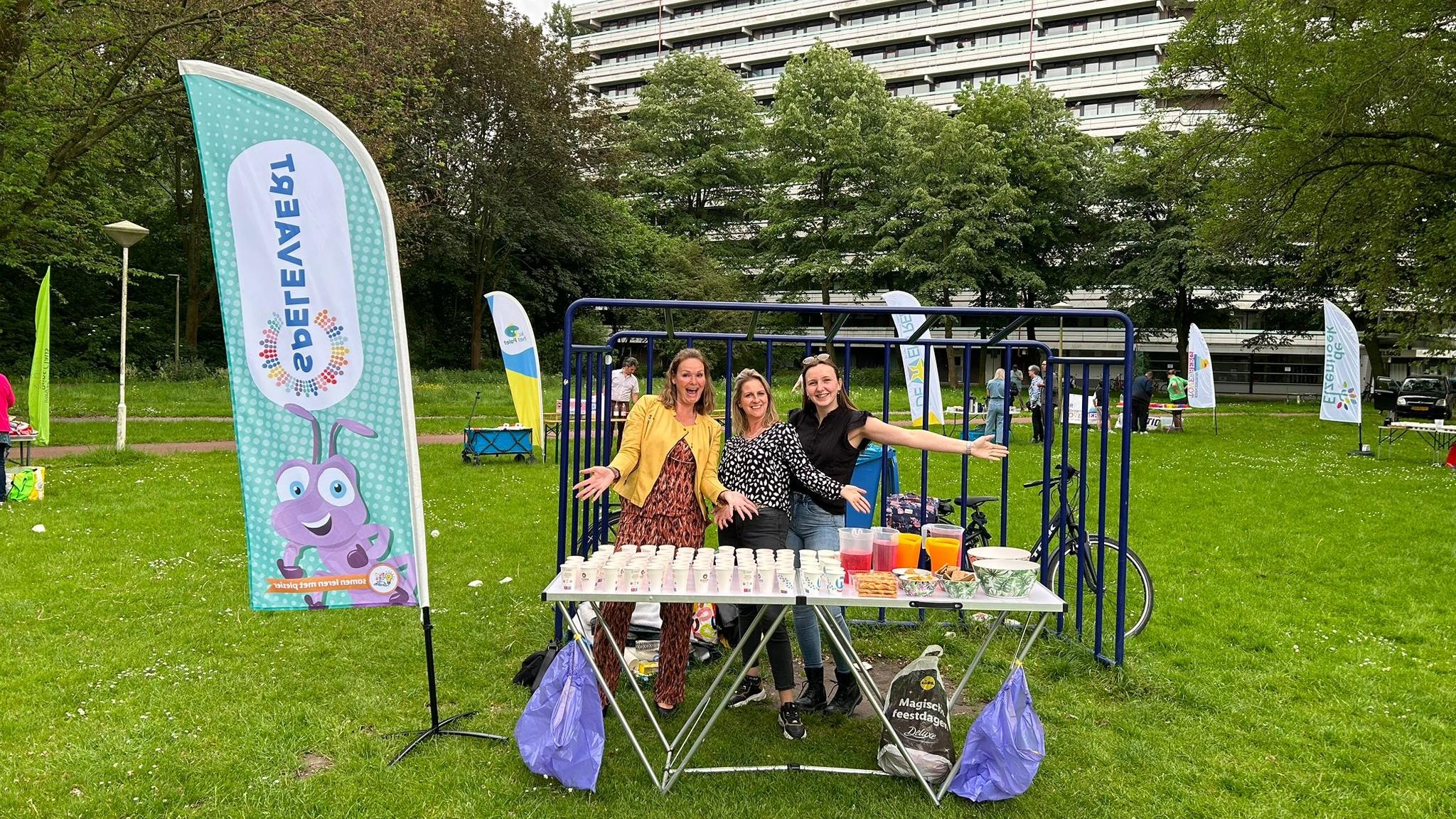 Drie vrolijke medewerkers van Kindcentrum De Spelevaert in Zoetermeer staan achter een tafel met drankjes op het schoolplein. Drie vrolijke medewerkers van Kindcentrum De Spelevaert in Zoetermeer staan achter een tafel met drankjes op het schoolplein.