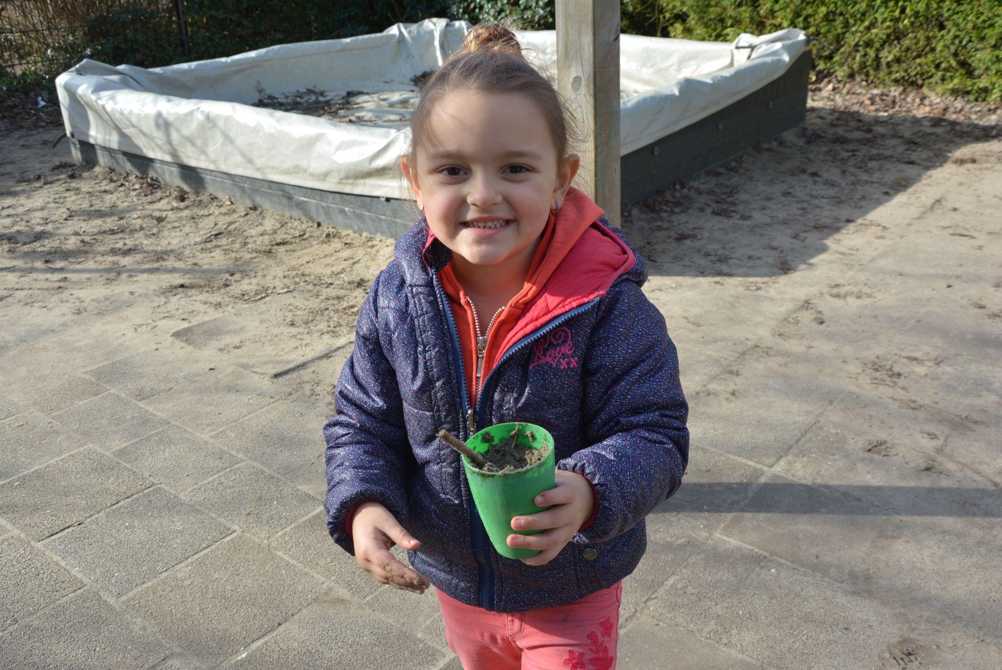 Een blij meisje op het schoolplein van CBS De Klimop in Ridderkerk met een groene beker vol zand. Een blij meisje op het schoolplein van CBS De Klimop in Ridderkerk met een groene beker vol zand.