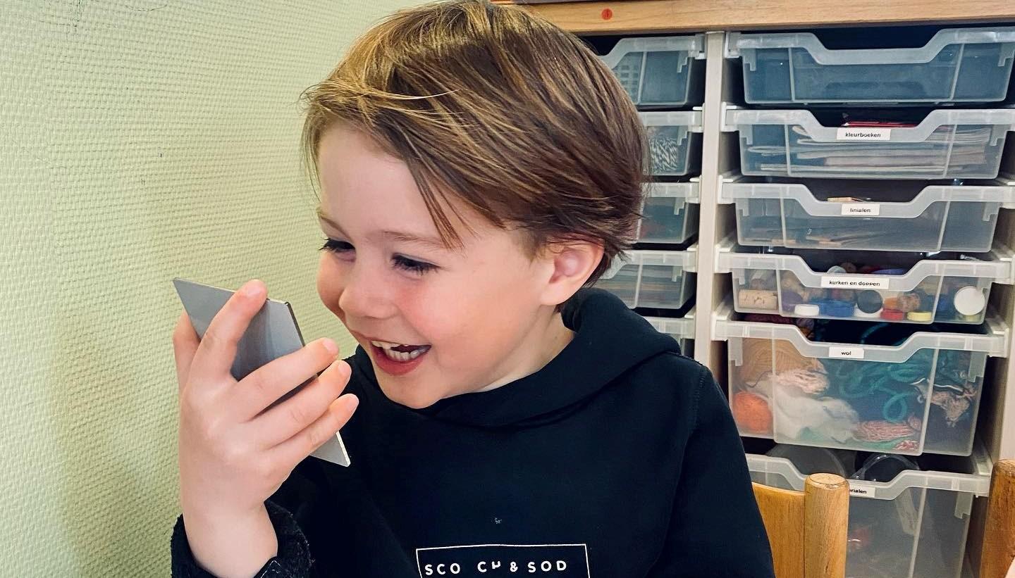 Een blije jongen in de klas van de Vrije School Stella Maris in Den Burg die enthousiast met een mobiel apparaat speelt. Een blije jongen in de klas van de Vrije School Stella Maris in Den Burg die enthousiast met een mobiel apparaat speelt.