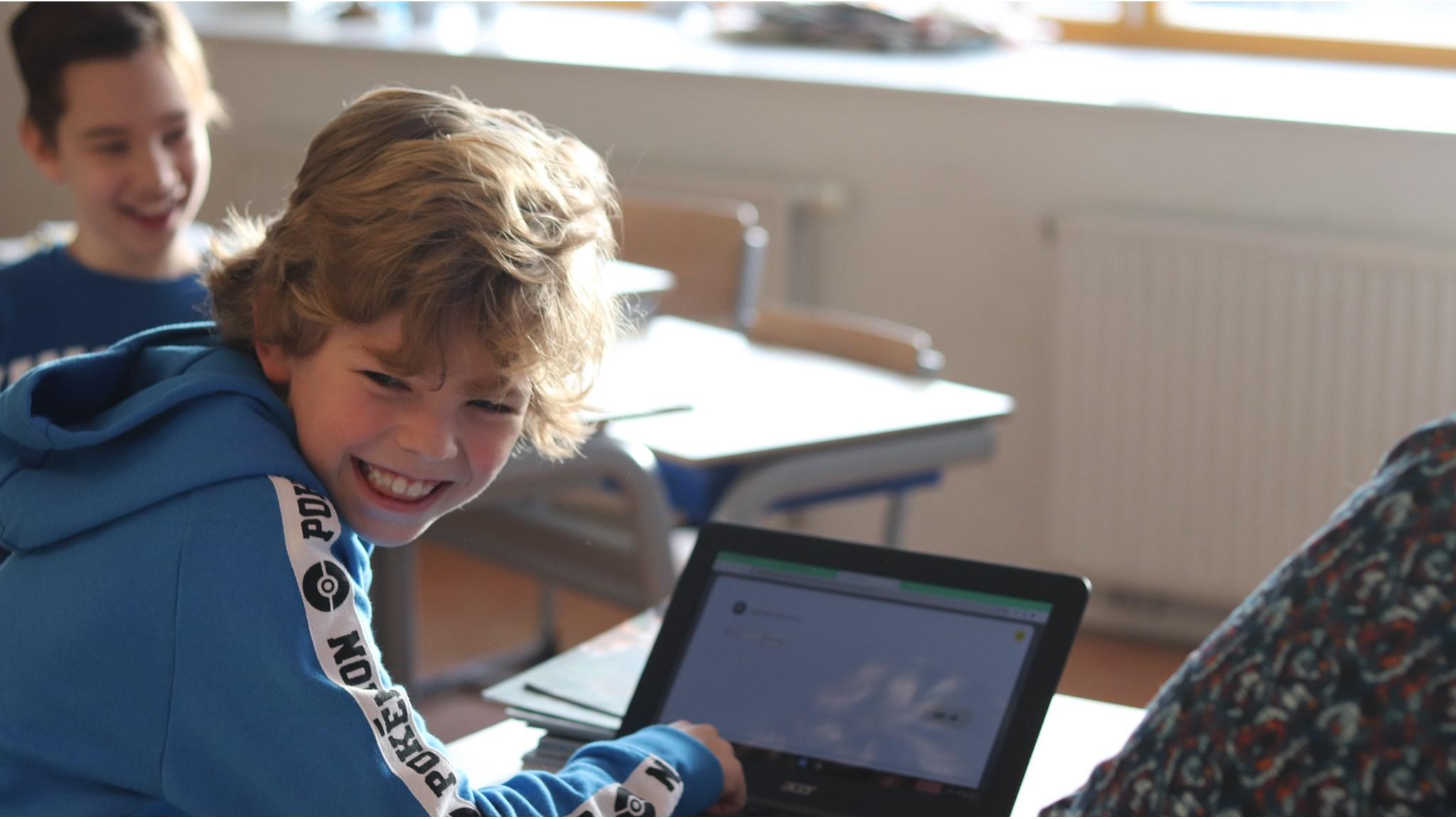 Een blije leerling achter een laptop in het klaslokaal van basisschool Opmaat in Nieuw-Vennep.
