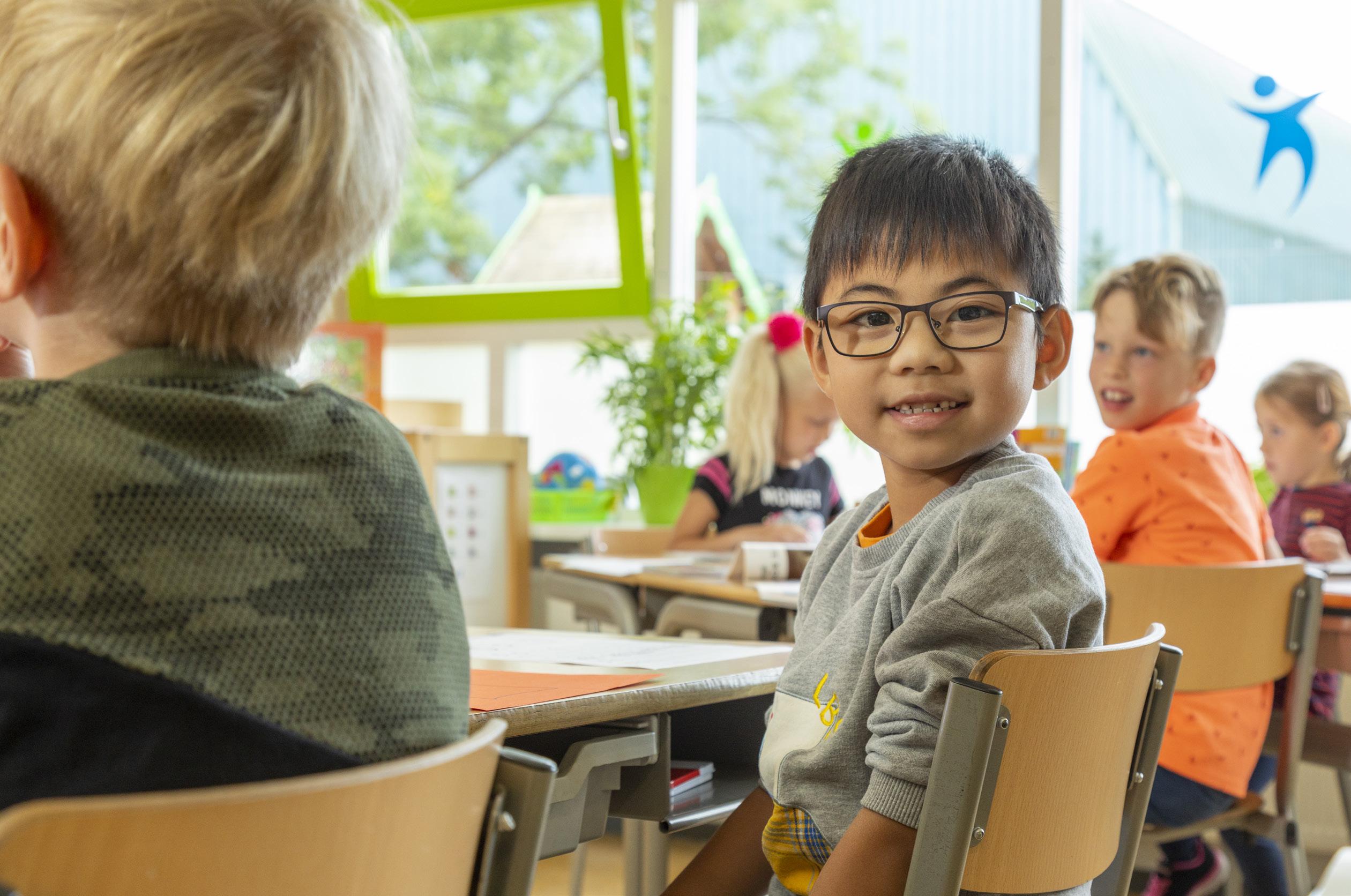 Een blije leerling van De Brug in IJsselstein zit aan zijn bureau in de klas.