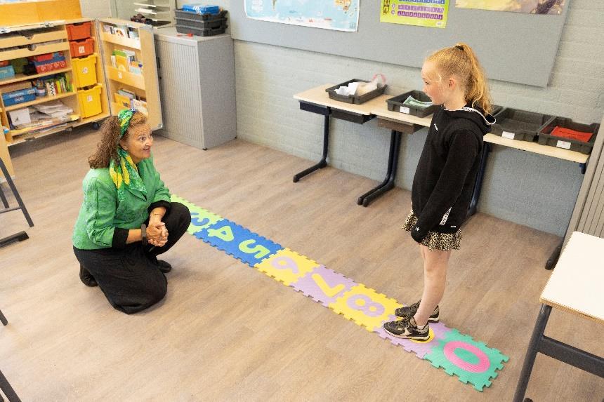 Een docente van de Prins Mauritsschool in De Lier staat knielend tegenover een leerling in een klaslokaal met kleurrijke puzzelmatten. Een docente van de Prins Mauritsschool in De Lier staat knielend tegenover een leerling in een klaslokaal met kleurrijke puzzelmatten.
