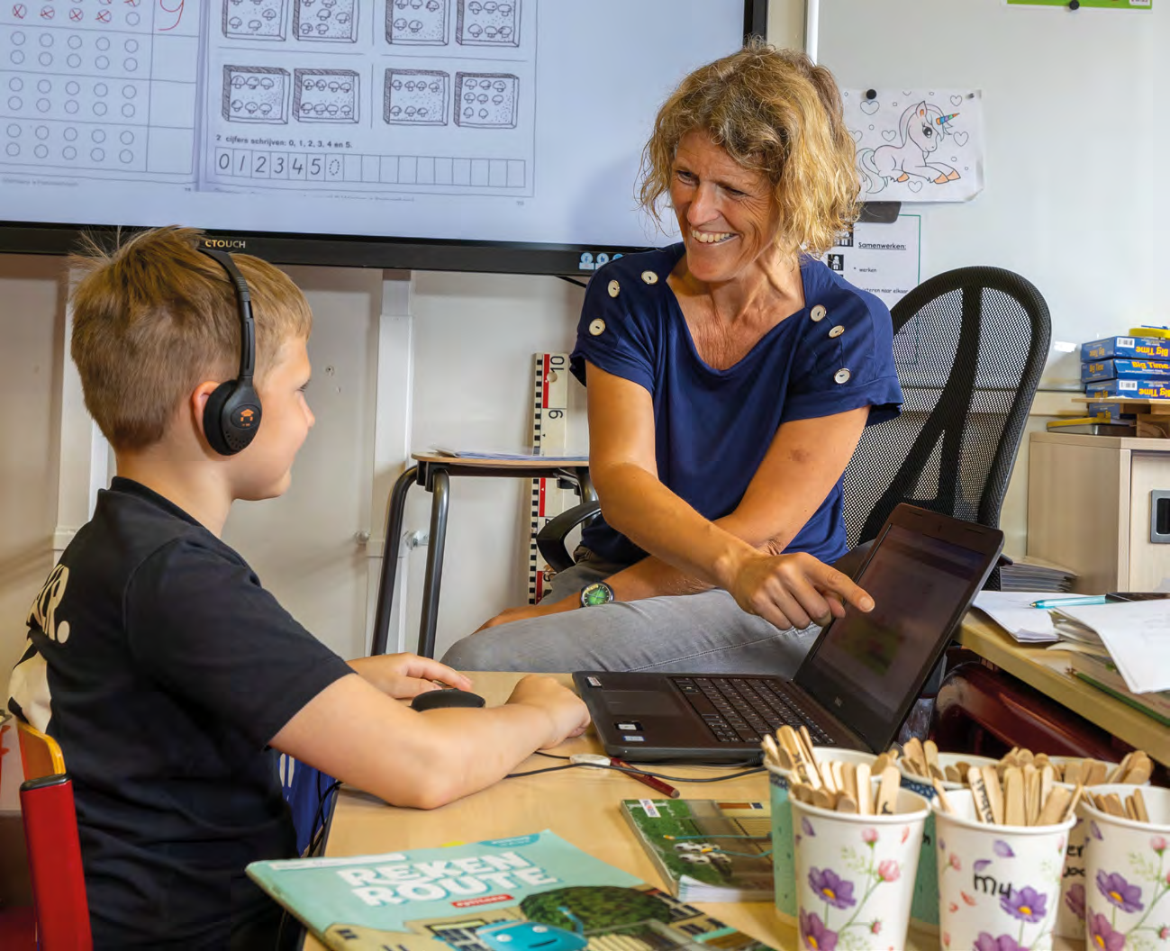 Een enthousiaste docente helpt een leerling met zijn laptop in het klaslokaal van De Springplank in Huizen. Een enthousiaste docente helpt een leerling met zijn laptop in het klaslokaal van De Springplank in Huizen.