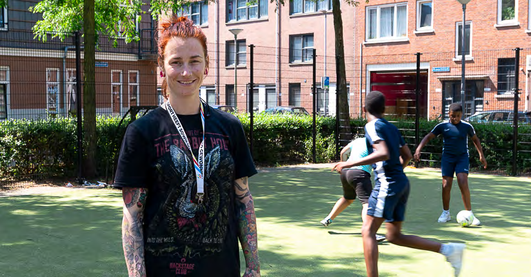 Een foto van een lerares op het schoolplein van CBS Mozaïek in Rotterdam met spelende kinderen.