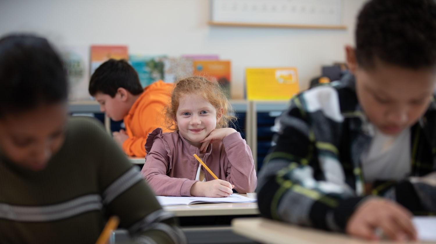 Een glimlachend meisje dat aan het schrijven is in de klas van School voor Speciaal Basisonderwijs De Kring in Rotterdam. Een glimlachend meisje dat aan het schrijven is in de klas van School voor Speciaal Basisonderwijs De Kring in Rotterdam.
