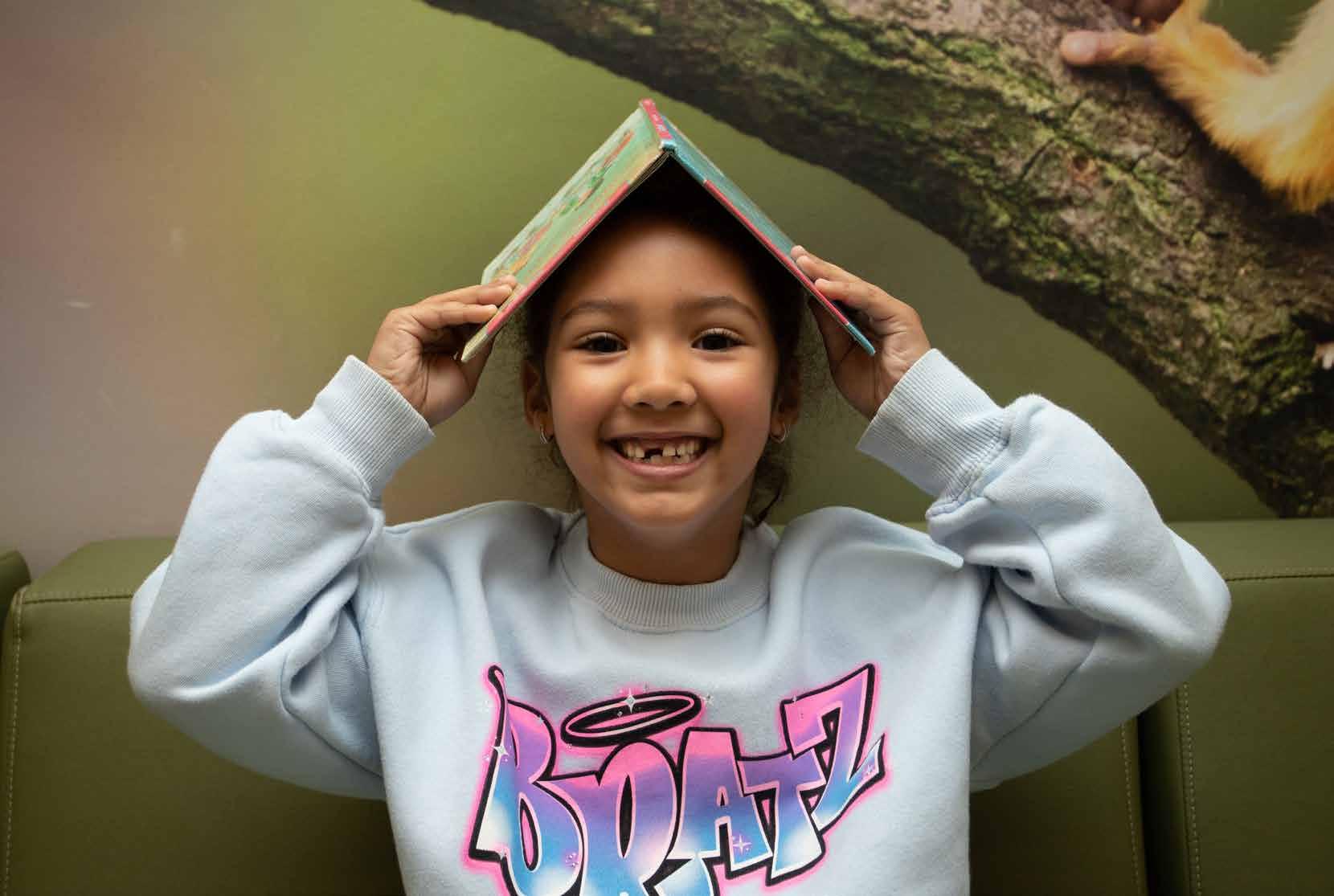 Een glimlachend meisje met een boek boven haar hoofd in de leeromgeving van basisschool Het Avontuur in Hoef en Haag.