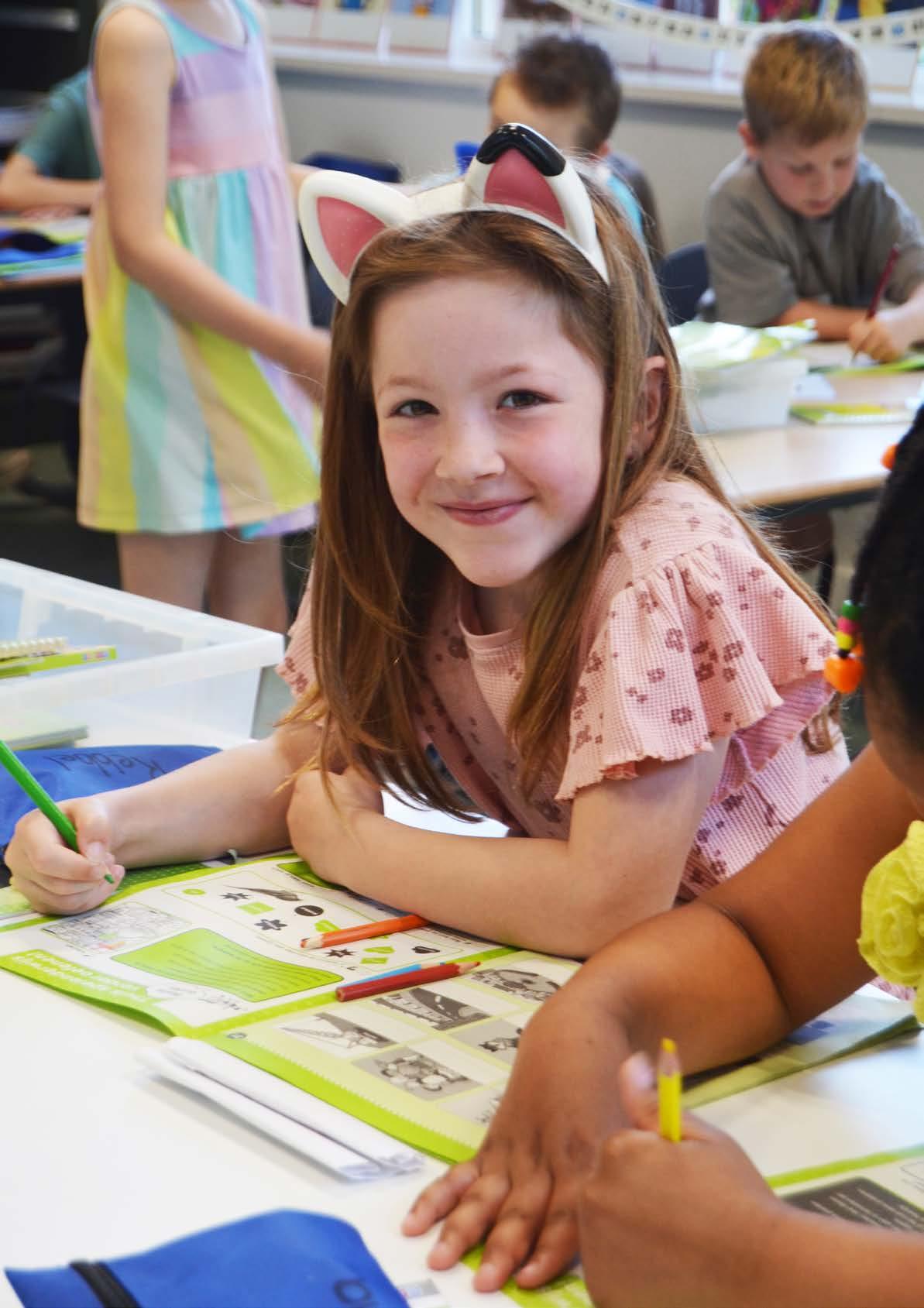 Een glimlachend meisje met een kattenoortjes-hoofdband werkt aan een schoolopdracht in Kindcentrum Theresia in Eindhoven. Een glimlachend meisje met een kattenoortjes-hoofdband werkt aan een schoolopdracht in Kindcentrum Theresia in Eindhoven.