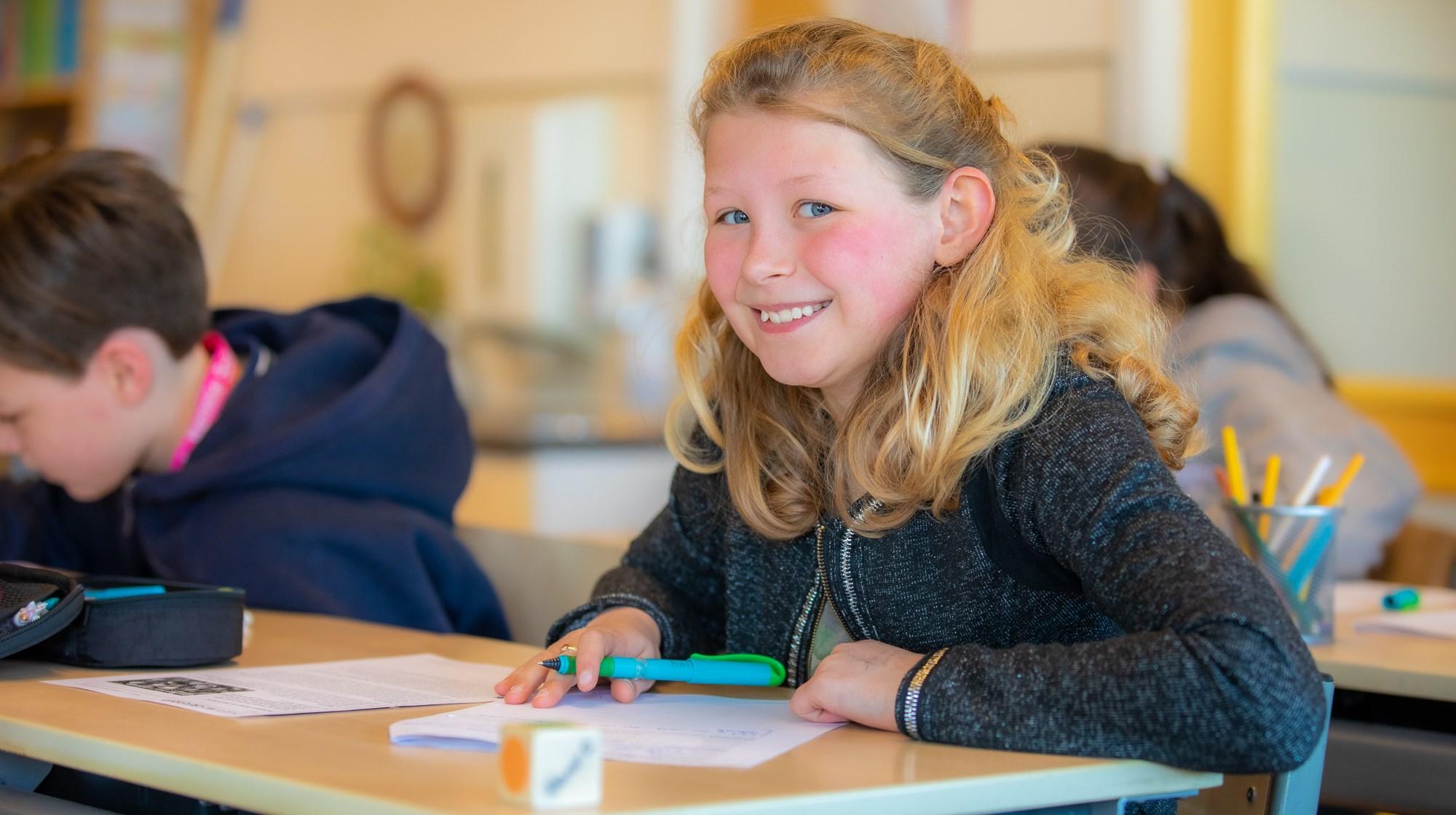 Een glimlachend meisje met krullend haar werkt aan een opdracht in de klas van De Gooise Daltonschool in Hilversum. Een glimlachend meisje met krullend haar werkt aan een opdracht in de klas van De Gooise Daltonschool in Hilversum.