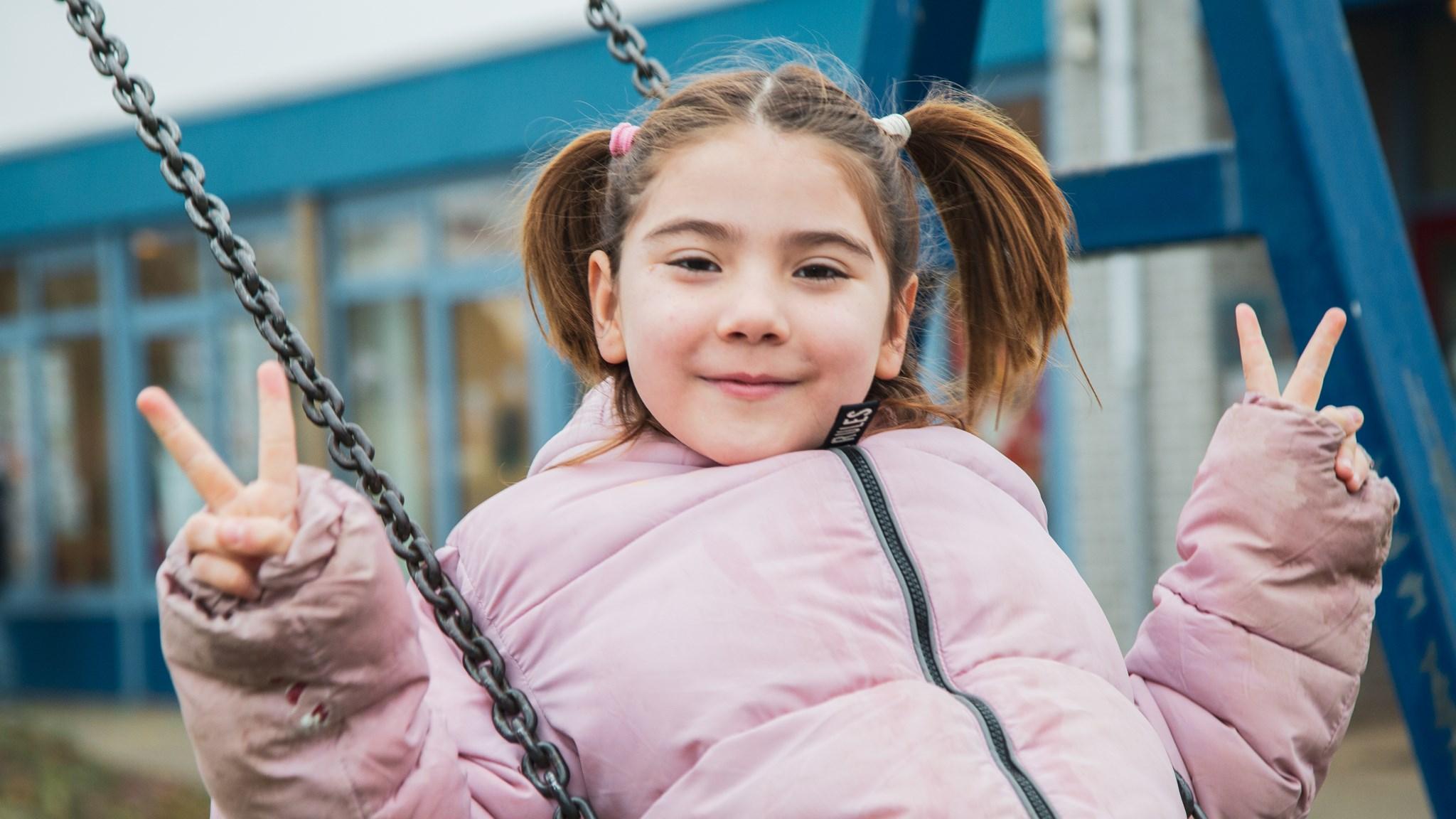 Een glimlachend meisje op de schommel op het schoolplein van RK Basisschool Schuttevaer in Hansweert.