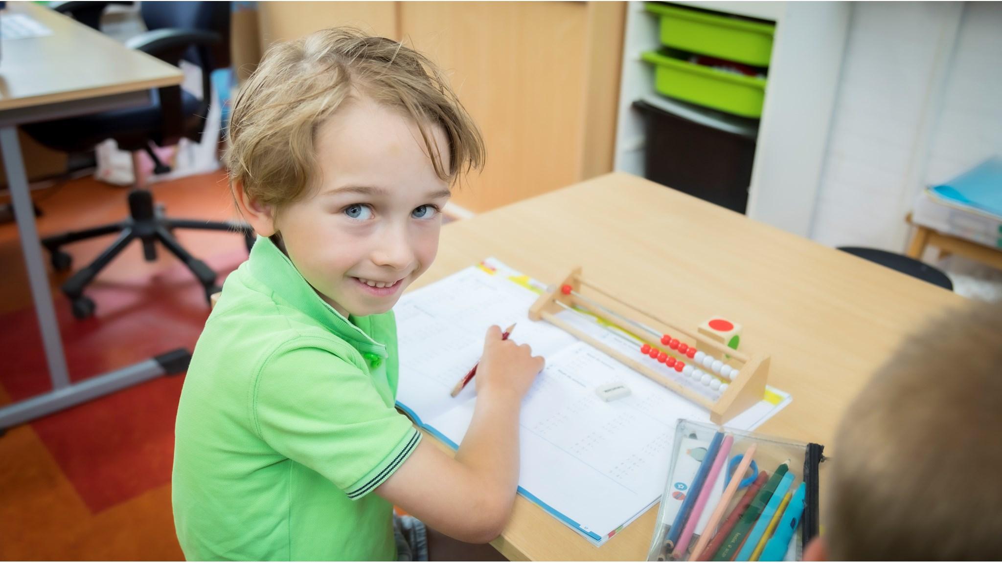 Een glimlachende jongen in een groene polo werkt aan zijn schoolwerk aan de Johan Frisoschool in Woerden. Een glimlachende jongen in een groene polo werkt aan zijn schoolwerk aan de Johan Frisoschool in Woerden.