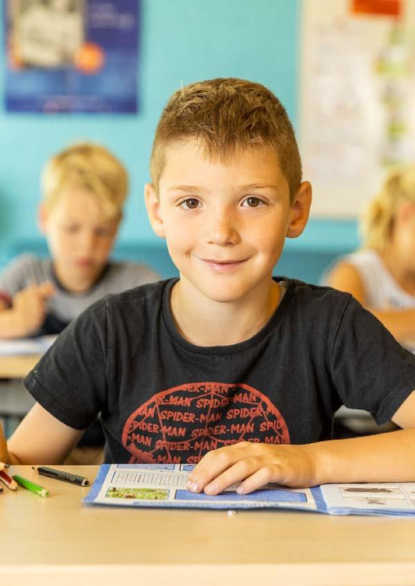 Een glimlachende jongen zit aan een bureau in de Eben Haezerschool in Oosterzee. Een glimlachende jongen zit aan een bureau in de Eben Haezerschool in Oosterzee.