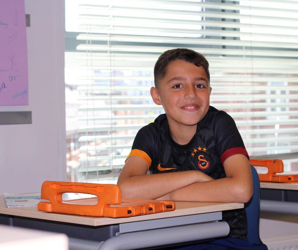 Een glimlachende jongen zit aan een bureau in het klaslokaal van de Prinses Marijkeschool in Den Haag. Een glimlachende jongen zit aan een bureau in het klaslokaal van de Prinses Marijkeschool in Den Haag.