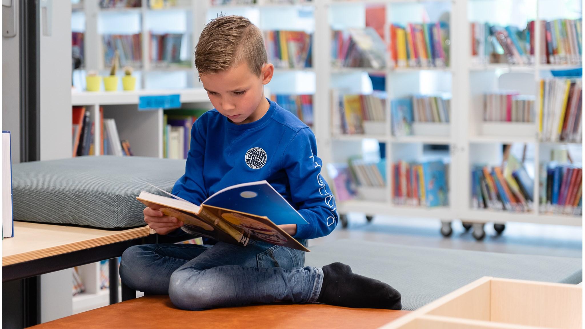 Een jongen leest een boek in de bibliotheek van Integraal Kind Centrum Het Klokhuis in Duiven. Een jongen leest een boek in de bibliotheek van Integraal Kind Centrum Het Klokhuis in Duiven.