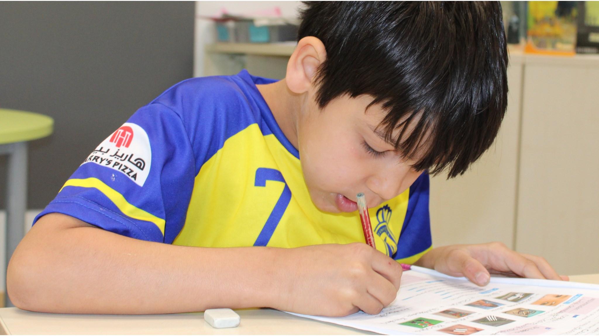 Een jongen schrijft met een potlood op een blad papier in de klas van Openbare Basisschool de Kraaienboom in Benningbroek. Een jongen schrijft met een potlood op een blad papier in de klas van Openbare Basisschool de Kraaienboom in Benningbroek.