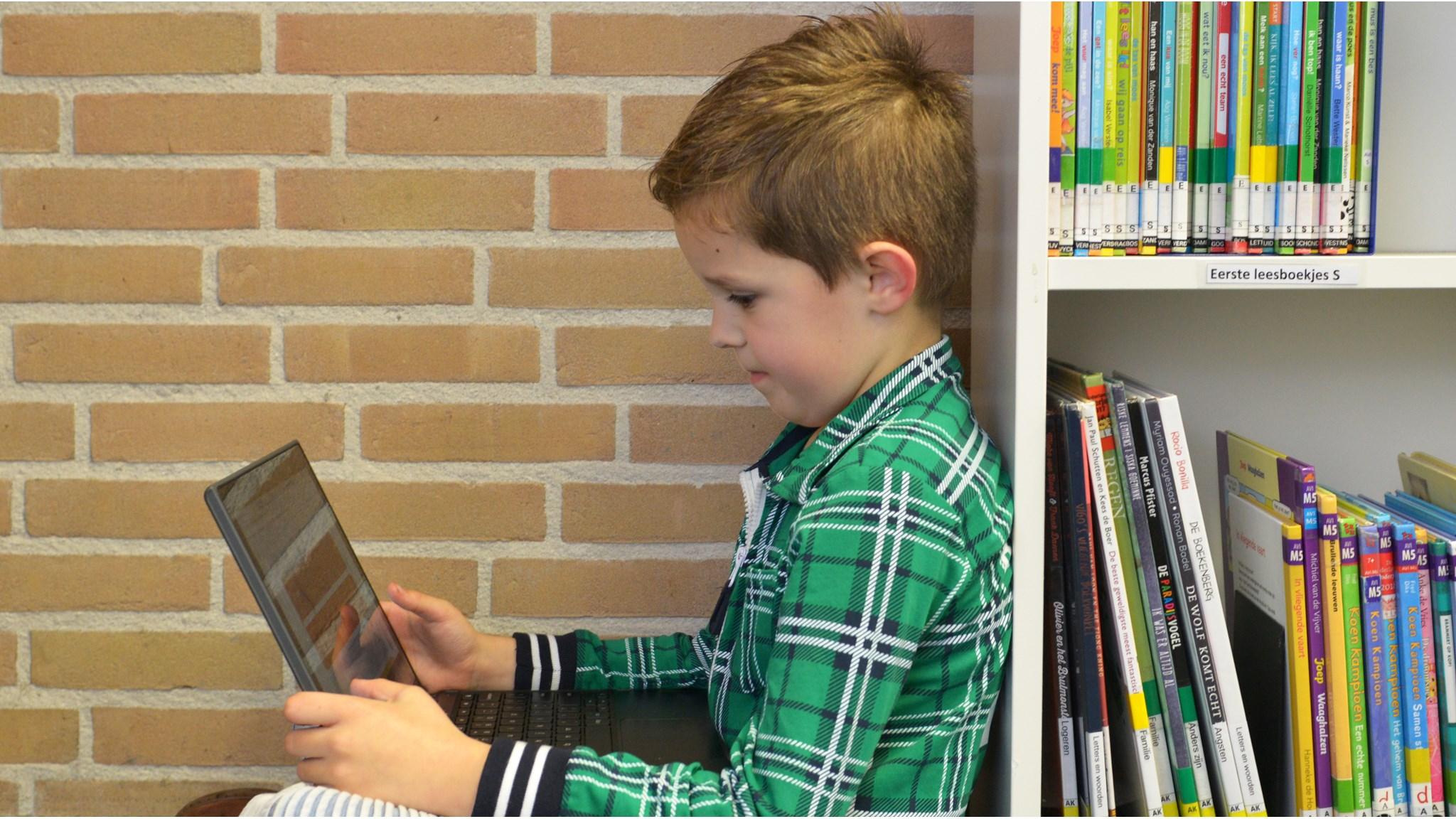 Een jongen werkt geconcentreerd op een laptop in de Mariaschool in Reutum, omringd door boeken. Een jongen werkt geconcentreerd op een laptop in de Mariaschool in Reutum, omringd door boeken.