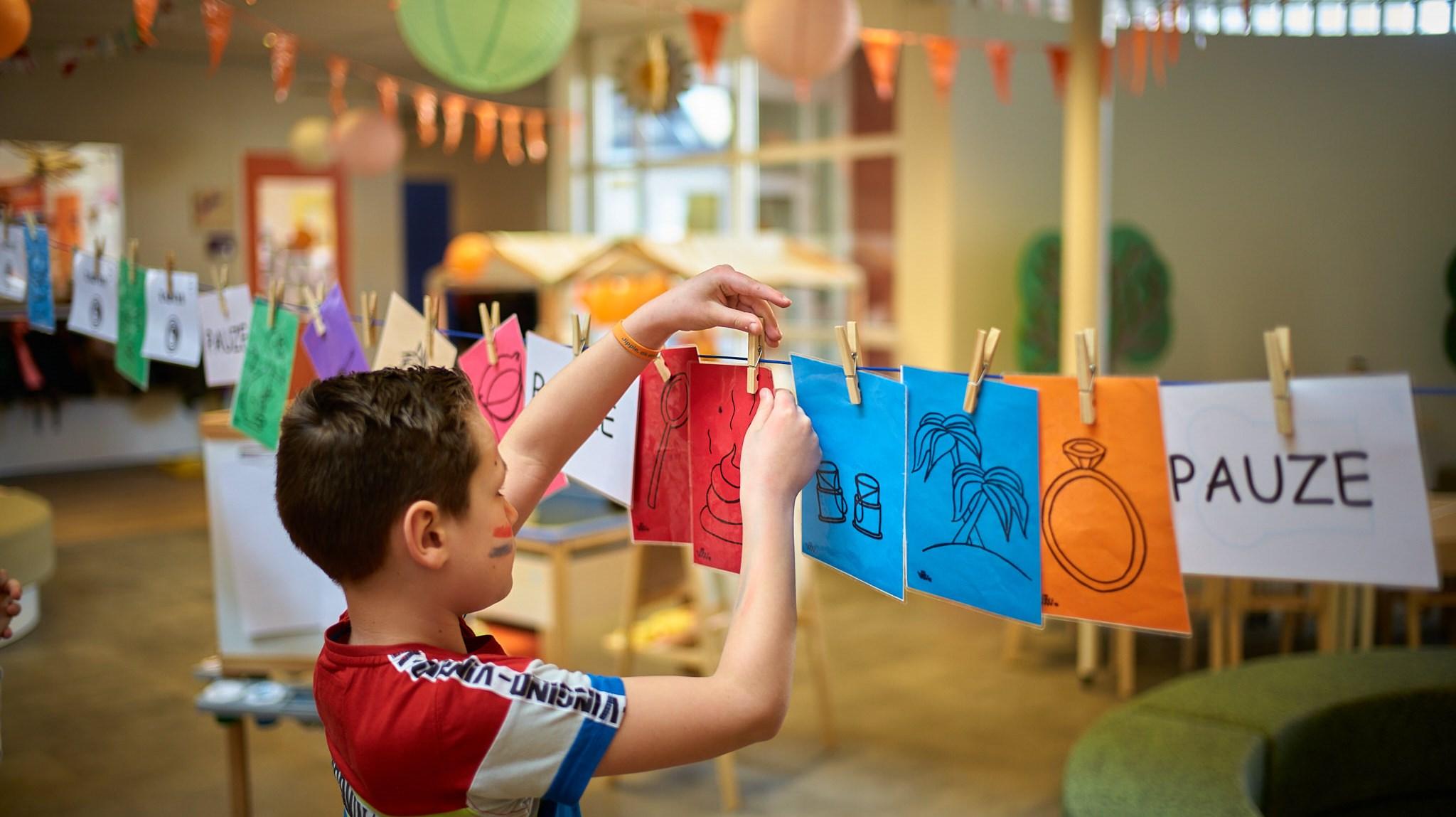 Een kind hangt kleurige tekeningen op in Basisschool De Krabbenkooi in Bergen op Zoom. Een kind hangt kleurige tekeningen op in Basisschool De Krabbenkooi in Bergen op Zoom.