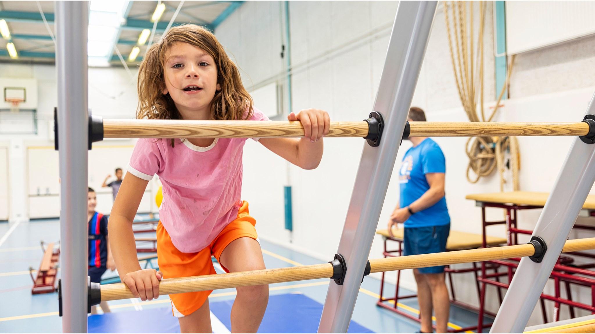 Een kind klimt enthousiast op de klimtoestellen in de gymzaal van SBO De Watertuin in Almere. Een kind klimt enthousiast op de klimtoestellen in de gymzaal van SBO De Watertuin in Almere.