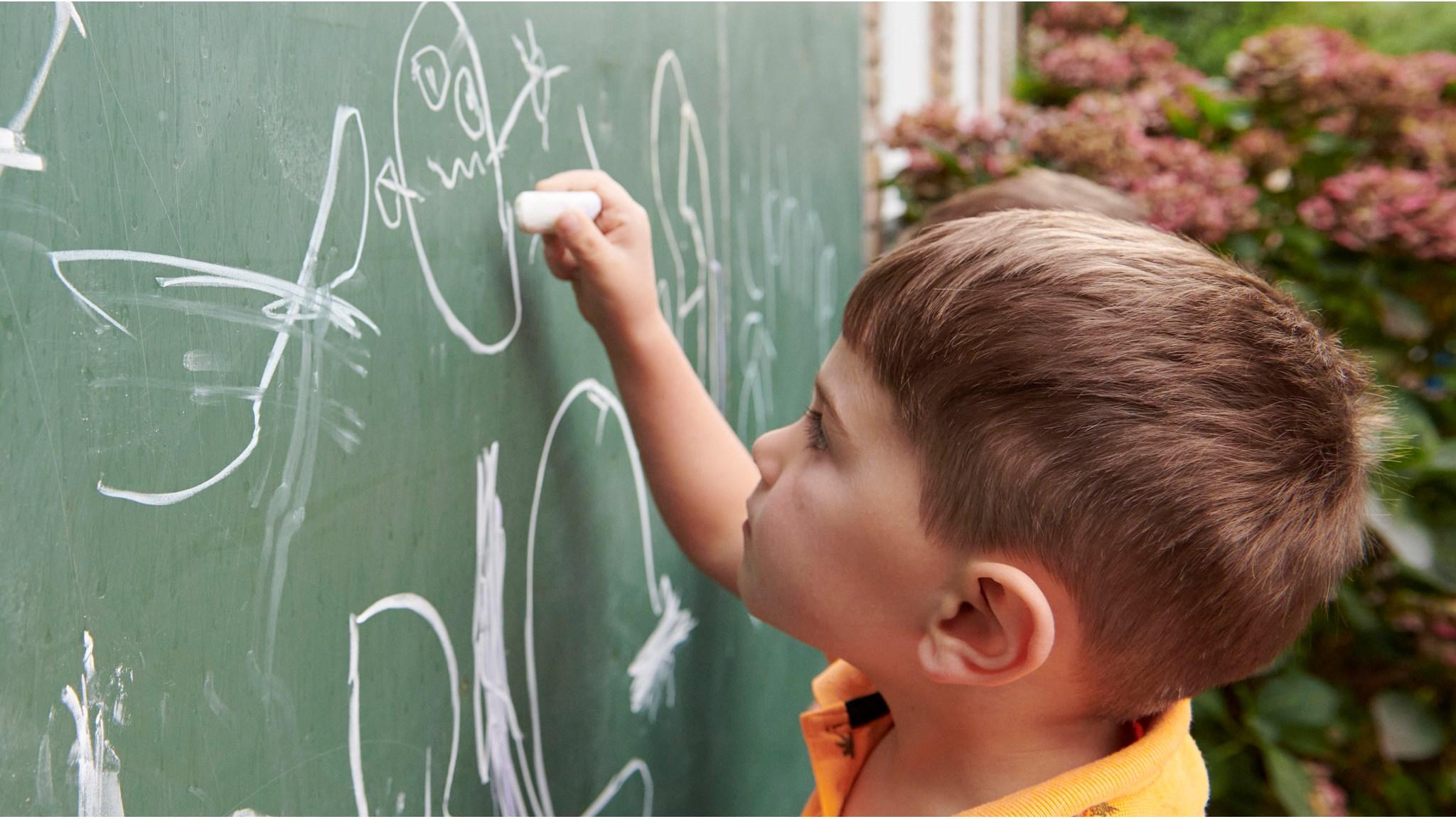 Een kind schrijft met krijt op een schoolbord op Openbare Basisschool De Wilgenhoek in Haarlem.