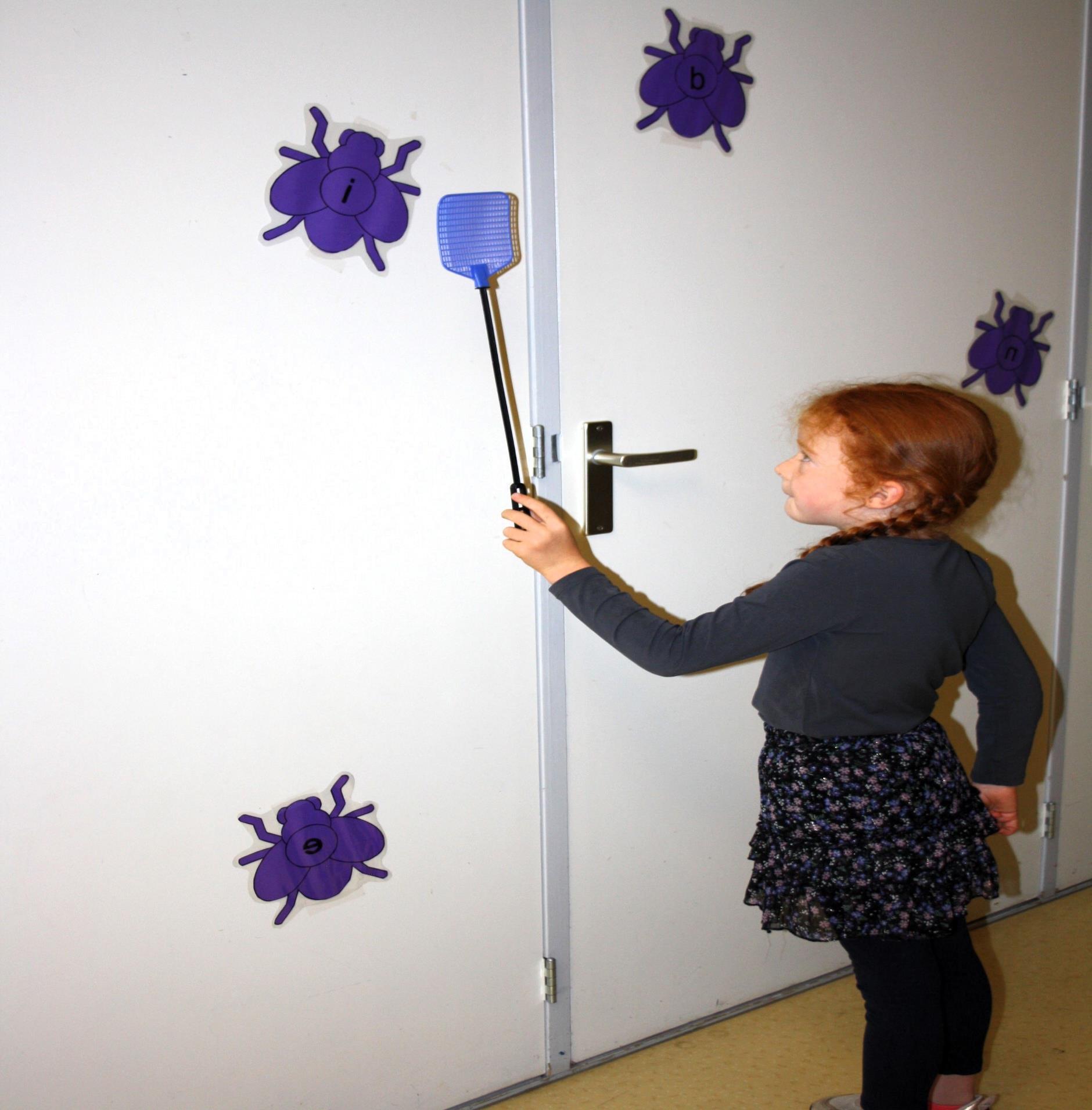 Een kind speelt met een vliegenmepper om op paarse insecten met letters te richten in Basisschool Jan Ligthart in Zelhem.