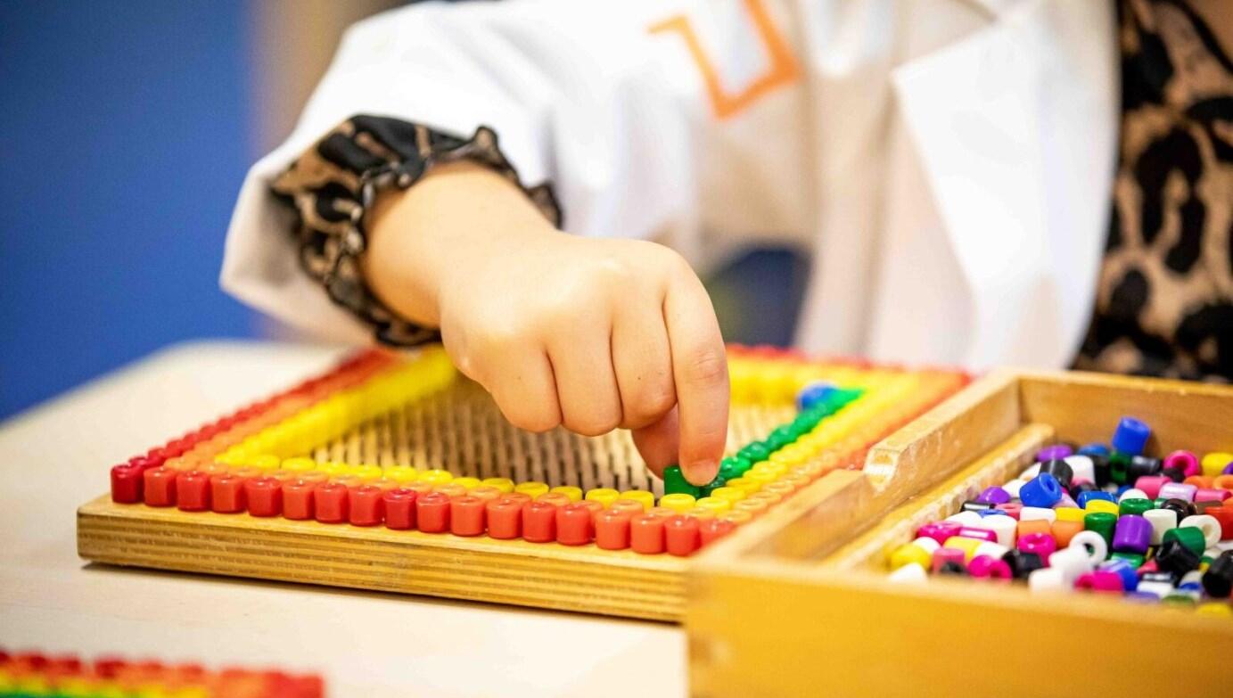 Een kind speelt met kleurrijke kralen op 't Ven van school 'Sterrenpad 't Ven' in Venlo.