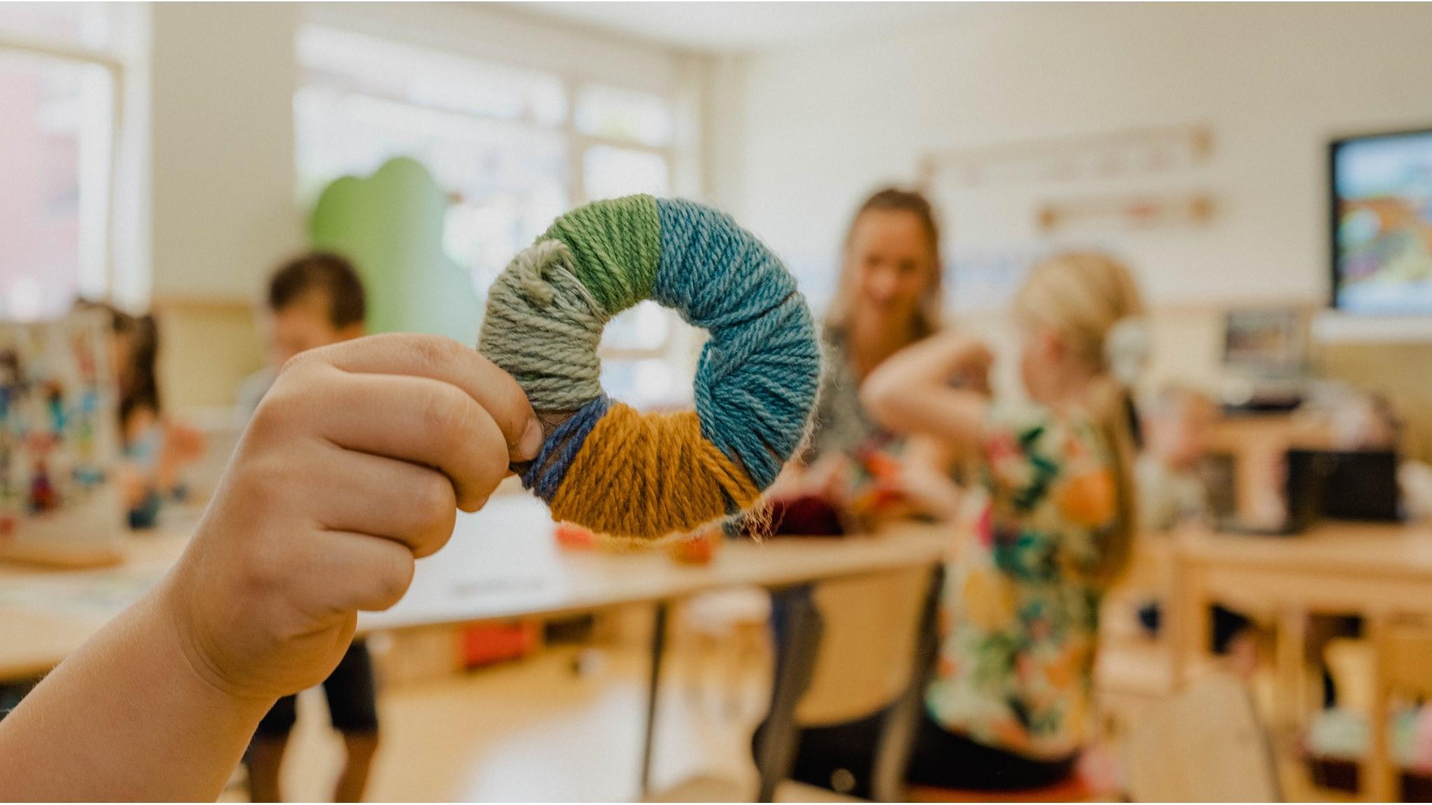 Een kind toont trots een kleurrijke wolring tijdens een creatieve activiteit op Basisschool Prins Willem-Alexander in Waarder. Een kind toont trots een kleurrijke wolring tijdens een creatieve activiteit op Basisschool Prins Willem-Alexander in Waarder.