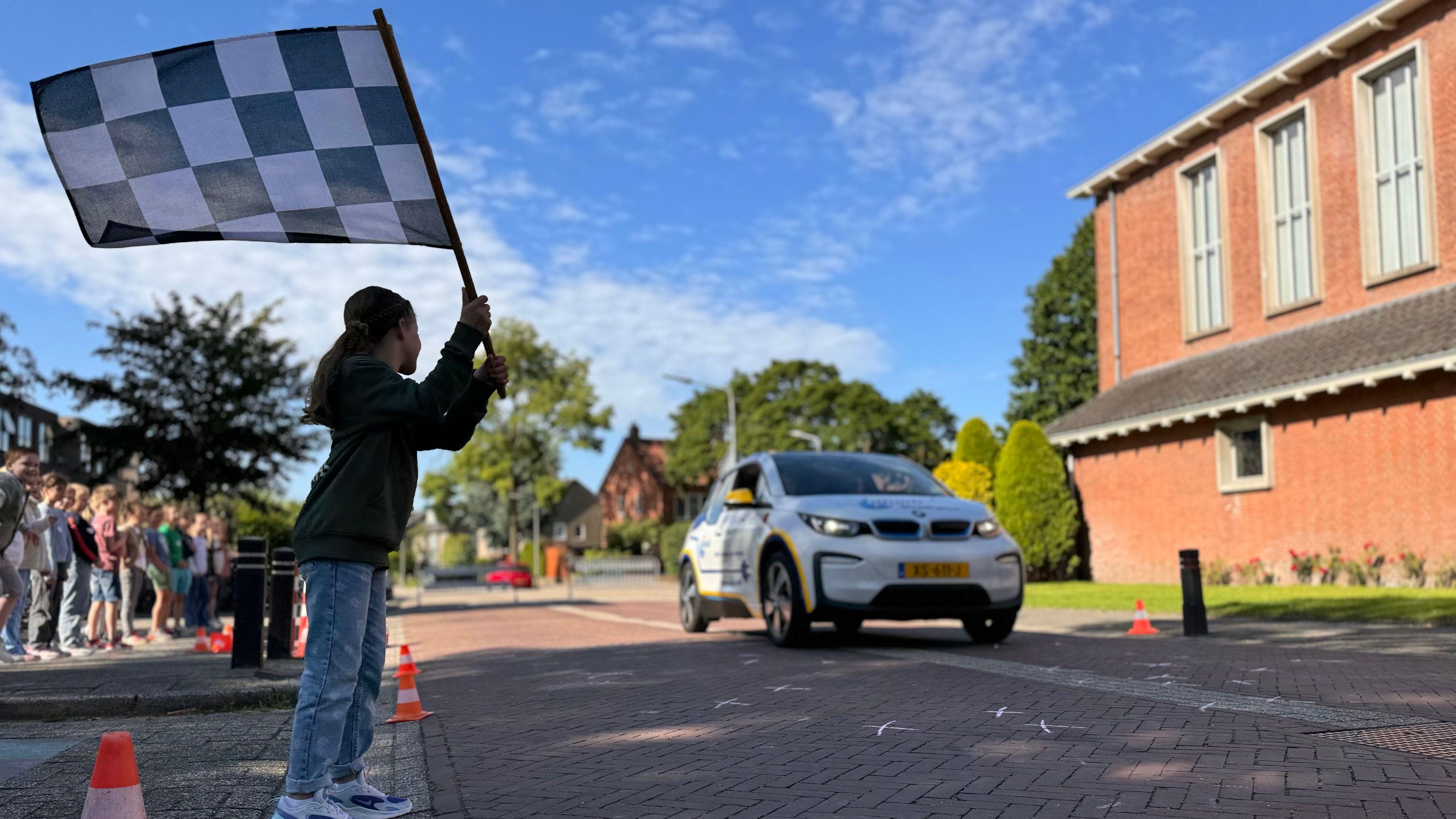 Een kind zwaait met een zwart-wit geblokte vlag voor een auto tijdens een activiteit op het schoolplein van Openbare Basisschool Elckerlyc in Hilversum. Een kind zwaait met een zwart-wit geblokte vlag voor een auto tijdens een activiteit op het schoolplein van Openbare Basisschool Elckerlyc in Hilversum.